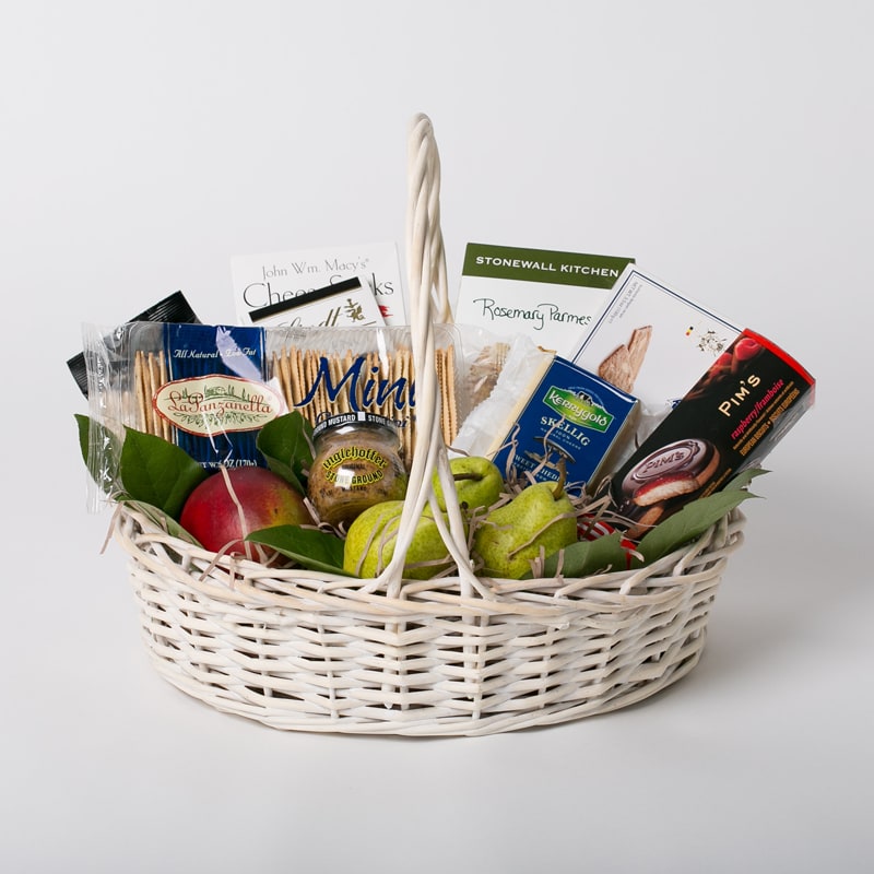 Gift basket with crackers, cheese, fruit, and packaged snacks in a white wicker basket