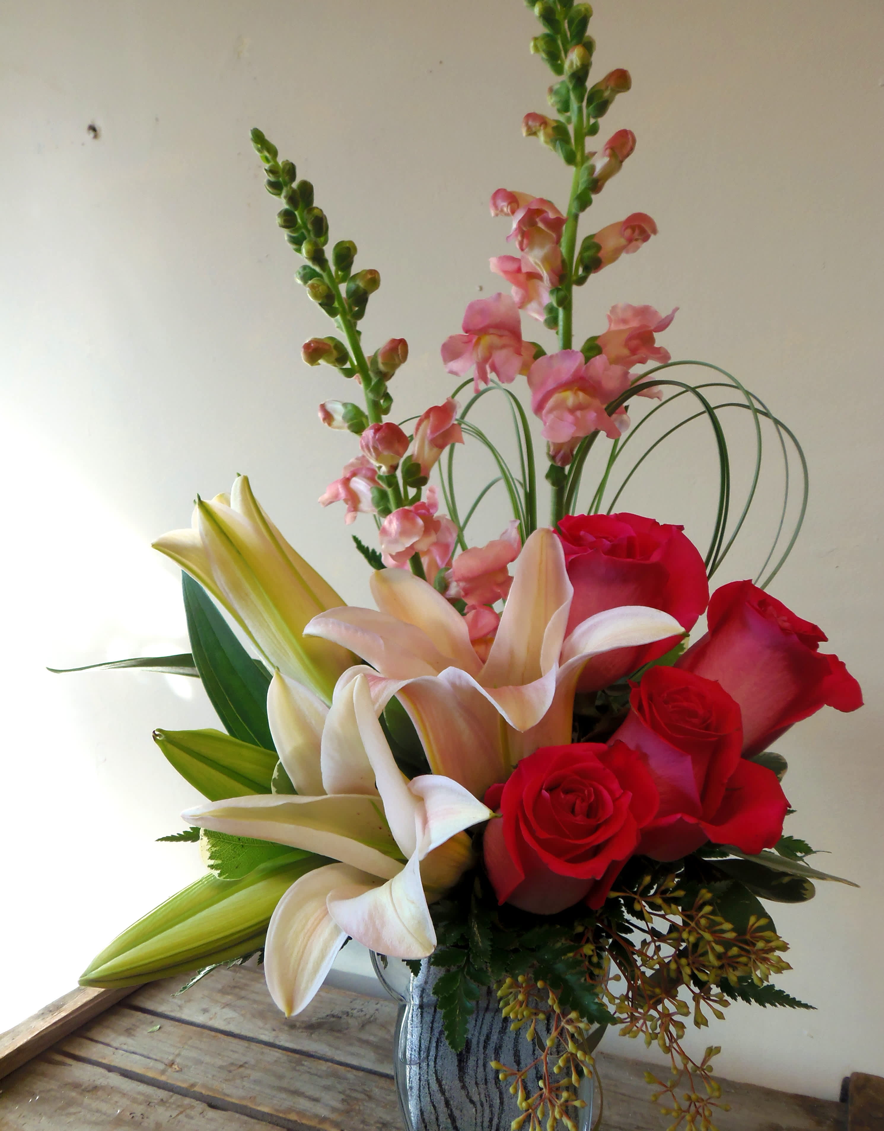 Bouquet of red roses, lilies, and pink snapdragons in a glass vase