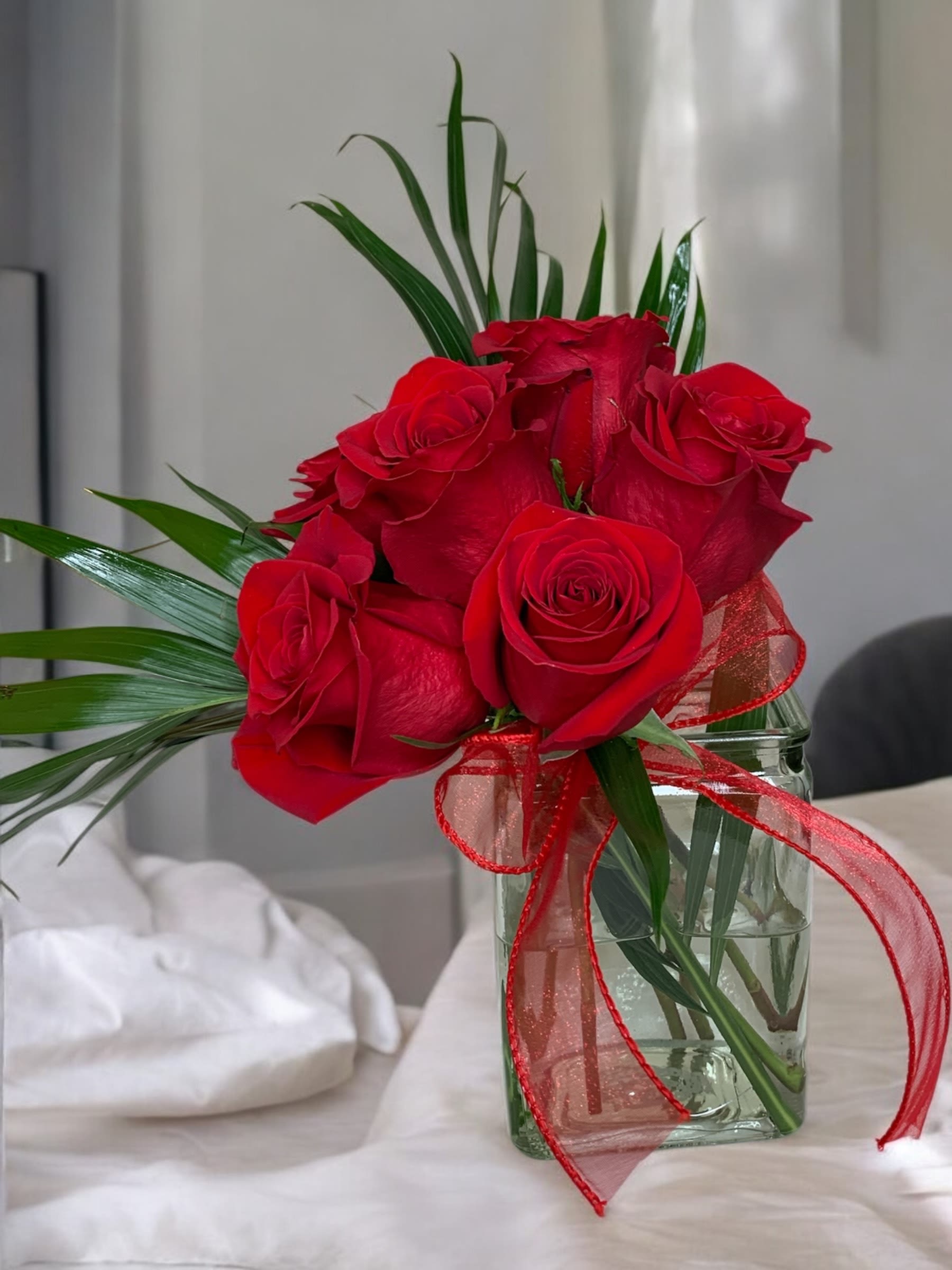 Red roses in a clear glass vase with a red ribbon