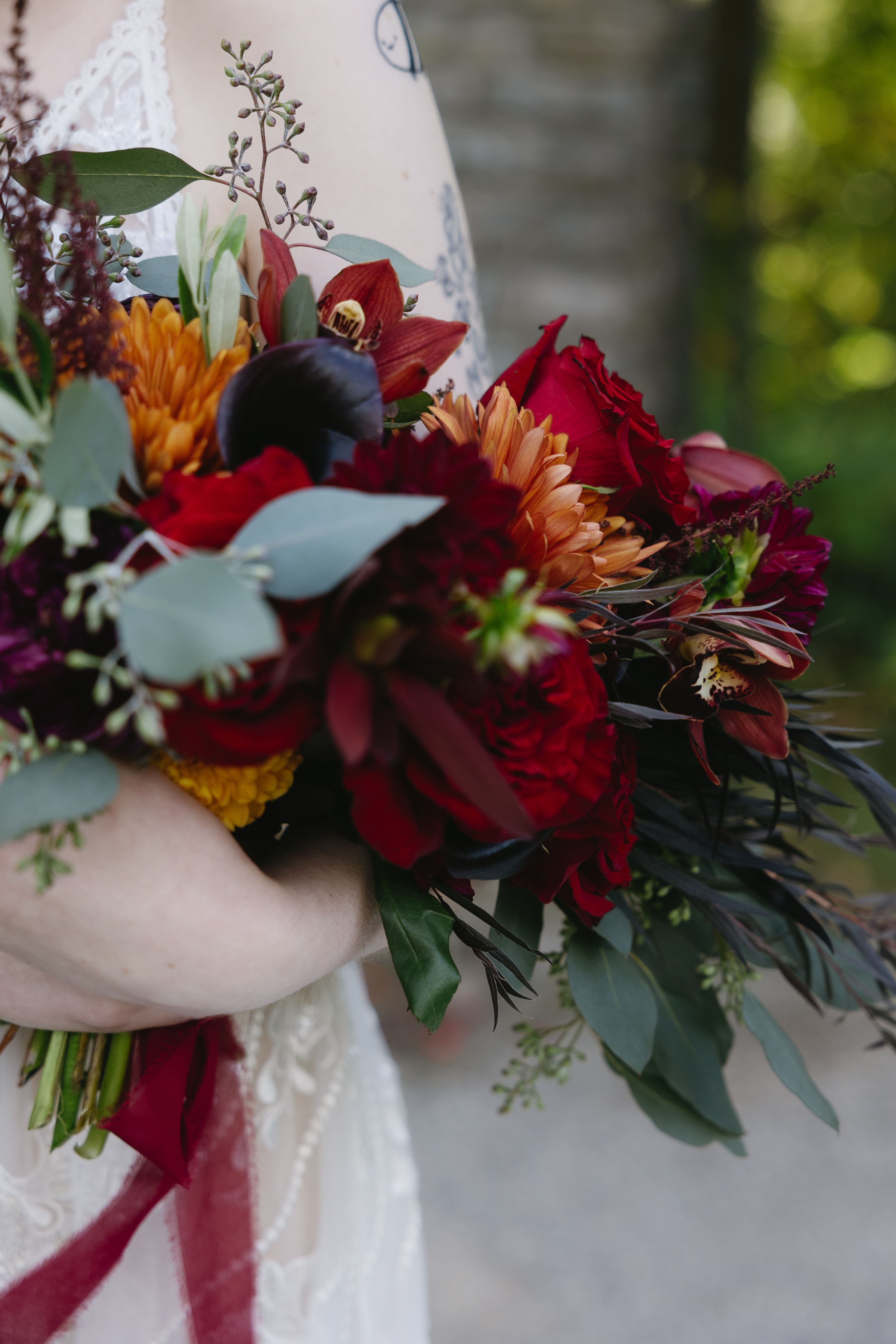 Bride holding a bouquet of red, orange, and burgundy flowers