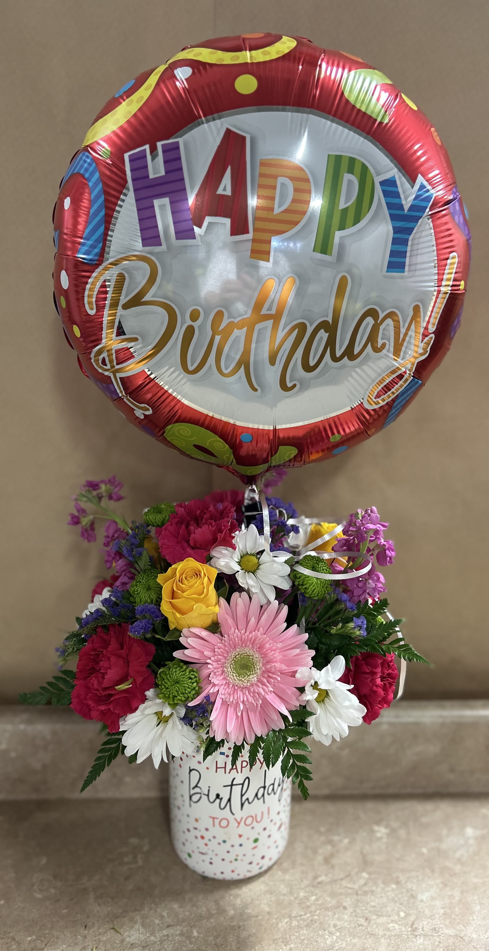 Birthday balloon above a mixed flower arrangement in a decorated cup