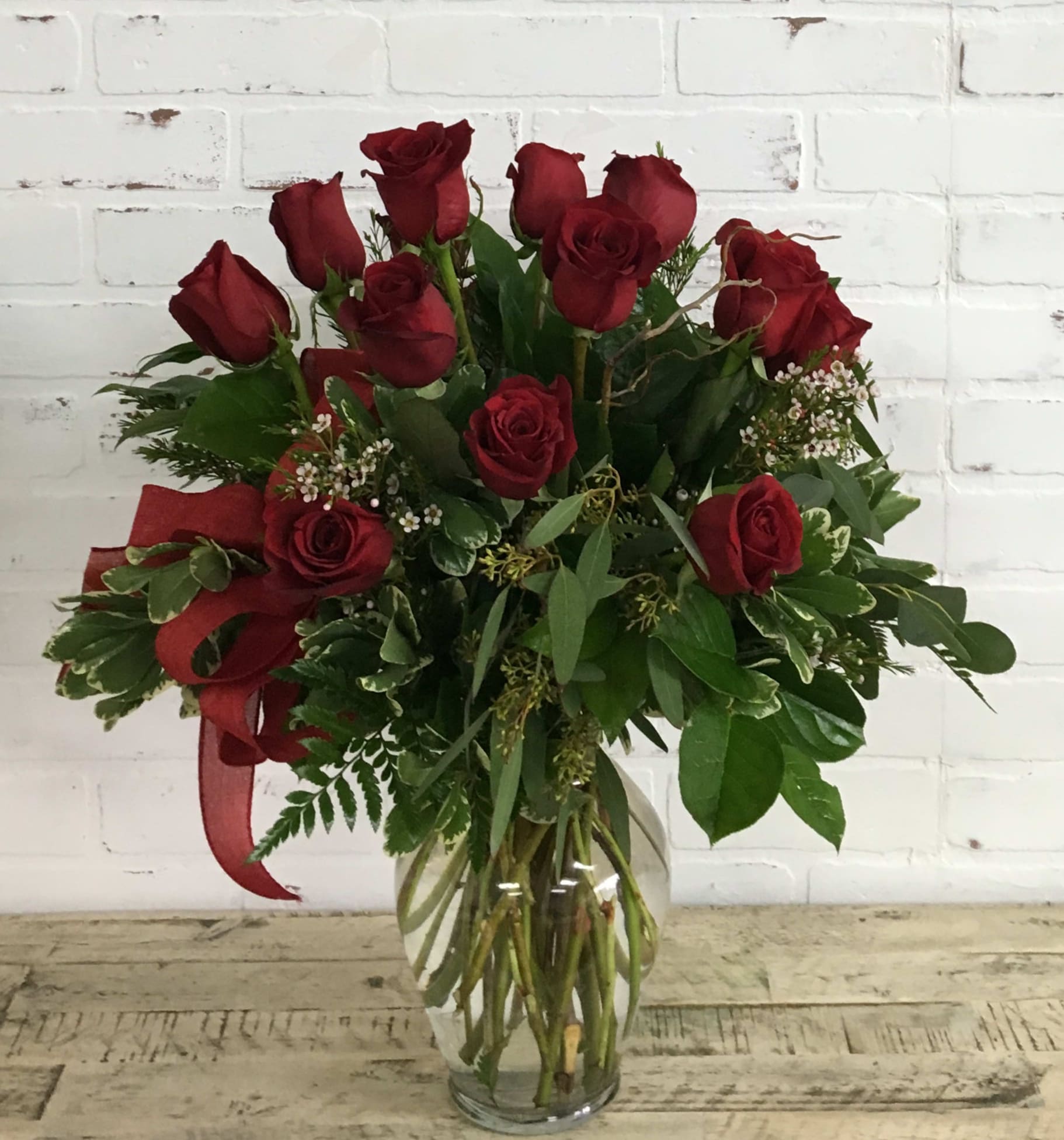 Red roses arranged in a clear glass vase with greenery and a red ribbon