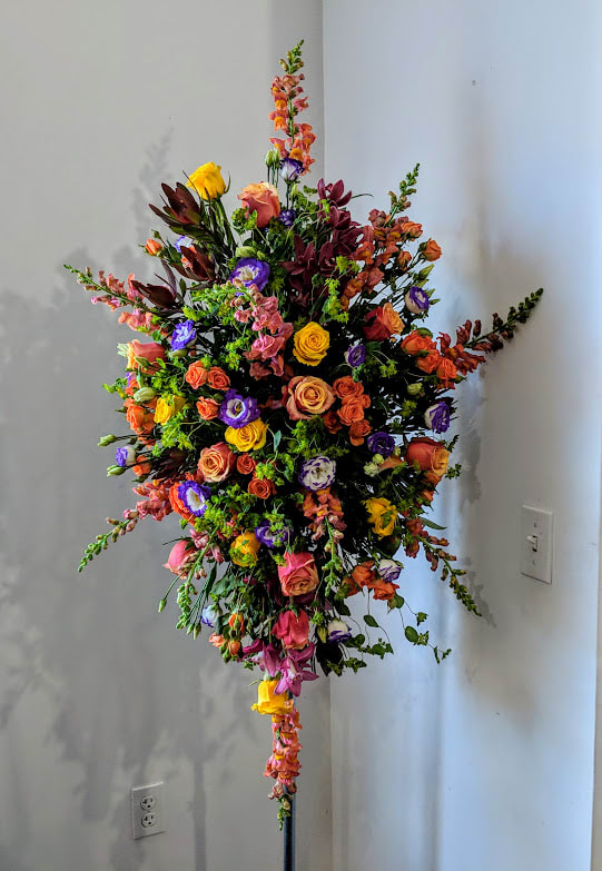 Tall multicolor standing spray with roses, lisianthus, and snapdragons on a black stand
