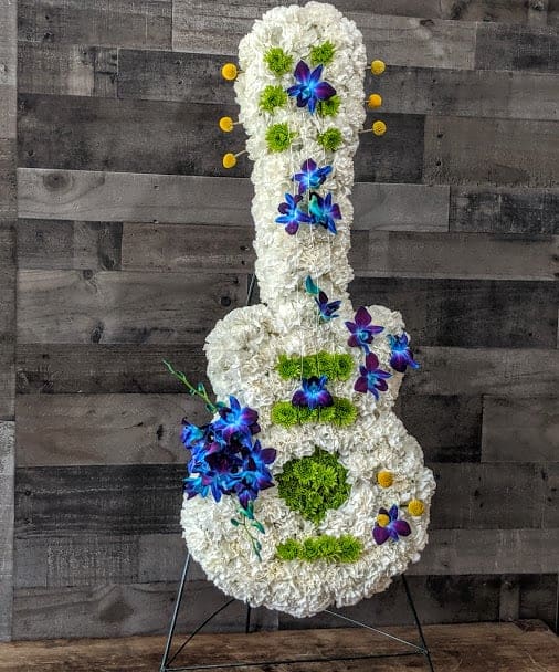 Tall guitar-shaped floral arrangement in white with blue orchids and green accents on a metal stand