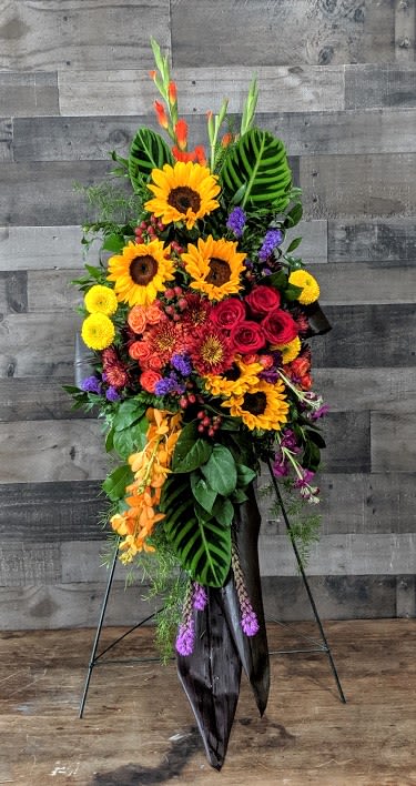 Tall standing spray of sunflowers, red roses, and bright mixed flowers on a metal easel.