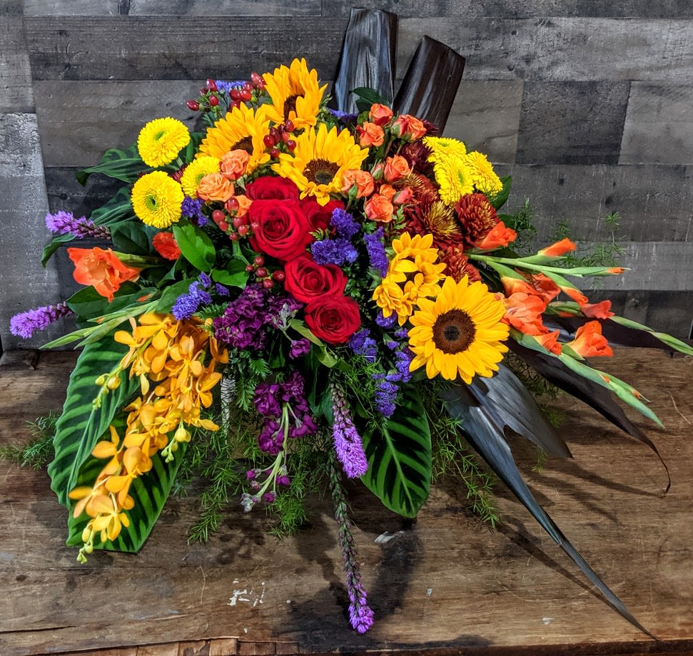 Vibrant horizontal arrangement with sunflowers, red roses, orchids and mixed flowers on a rustic wooden surface