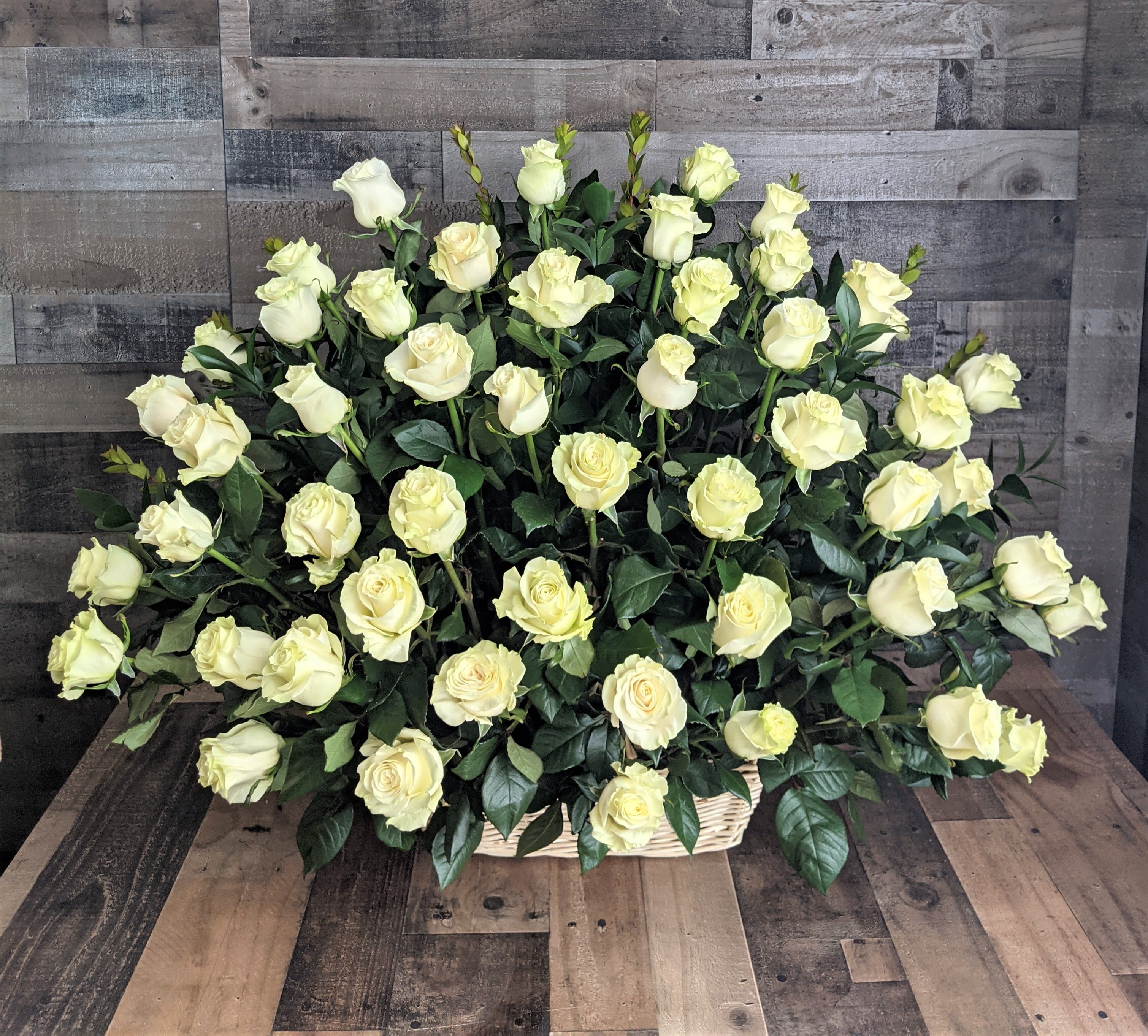 Large fan-shaped arrangement of ivory roses in a low wicker basket.