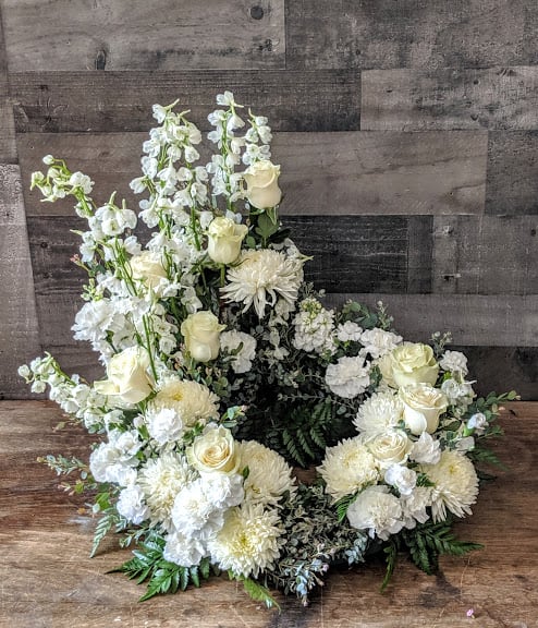 Open wreath of white and cream roses, mums, carnations, and tall white blooms arranged asymmetrically