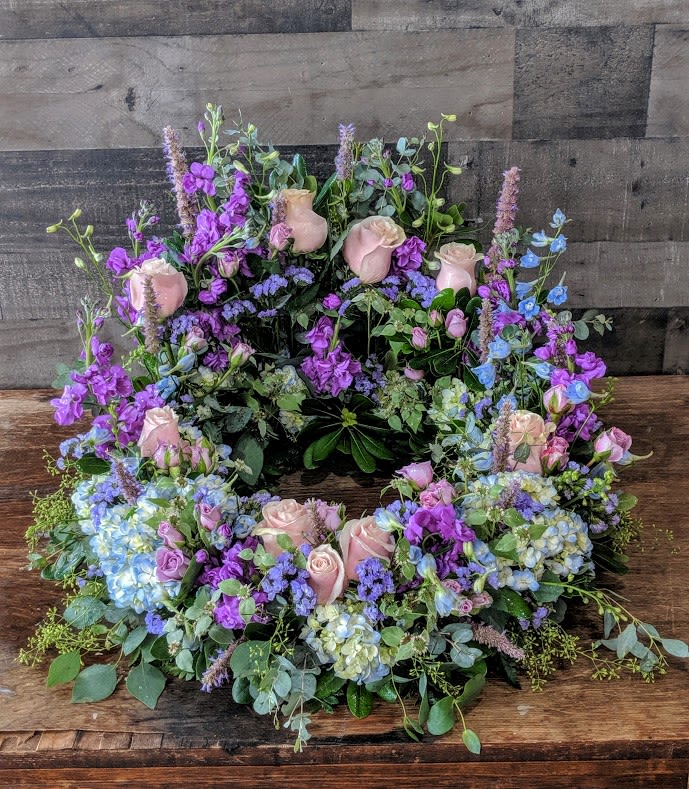 Pastel wreath of pink roses and purple and blue blooms arranged in a ring.