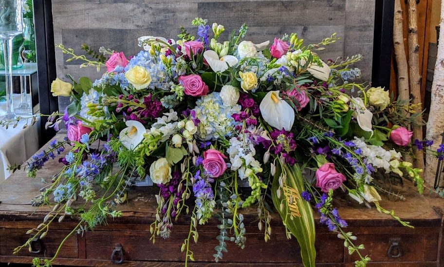 Low elongated arrangement of mixed pink, white, yellow, and blue flowers on a wooden surface