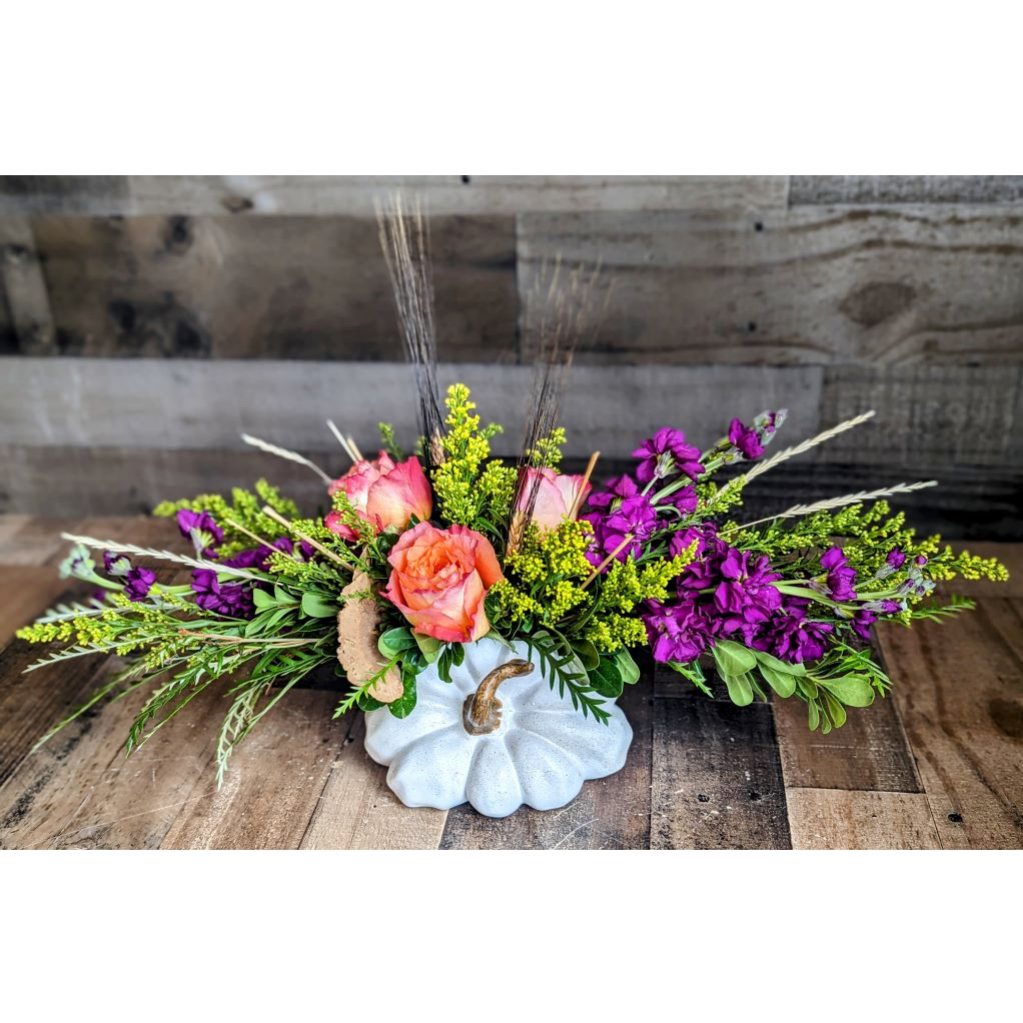 Low floral arrangement in a white pumpkin vase with pink roses and purple flowers