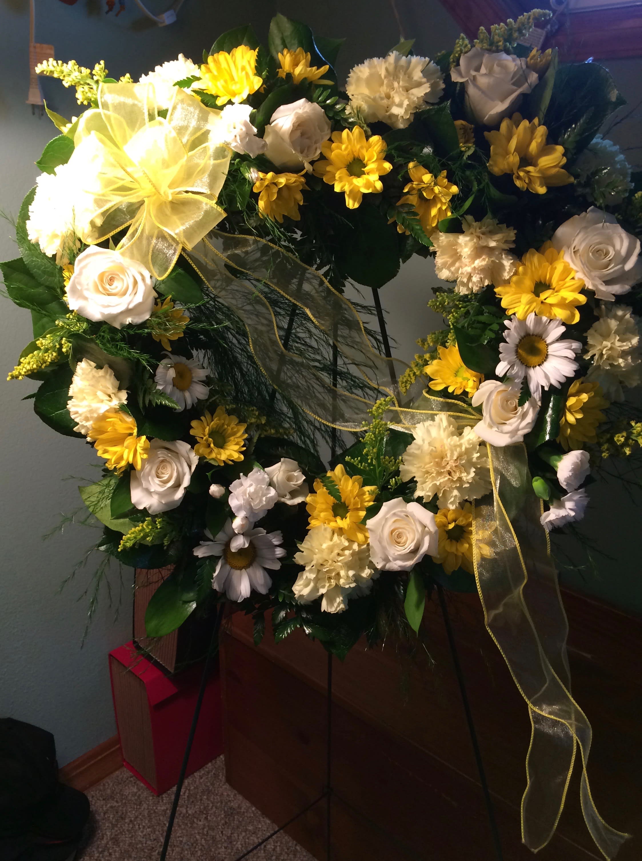 Heart-shaped floral wreath with white roses and yellow daisies on a stand