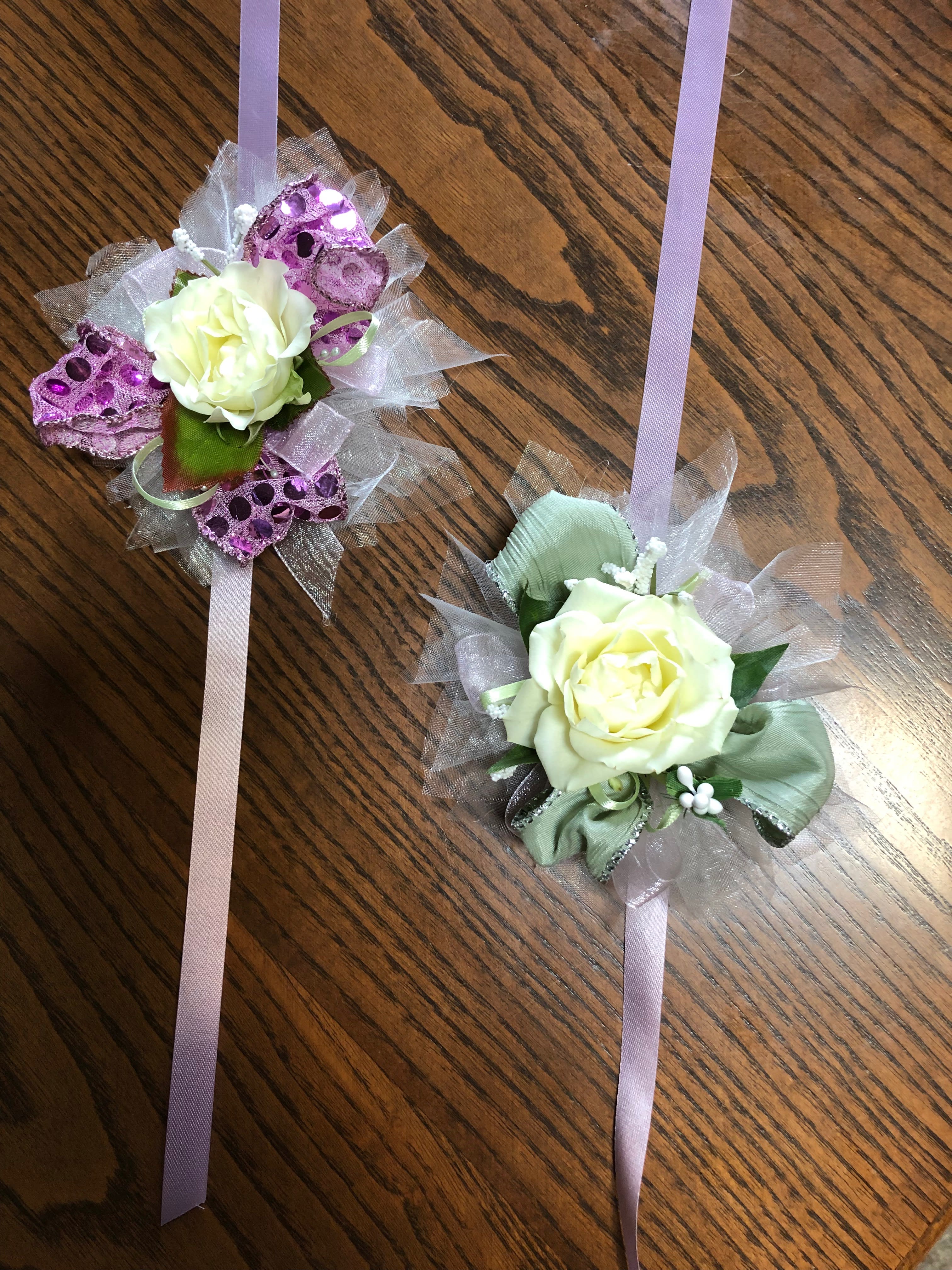 Two rose corsages with lavender ribbons on a wooden surface
