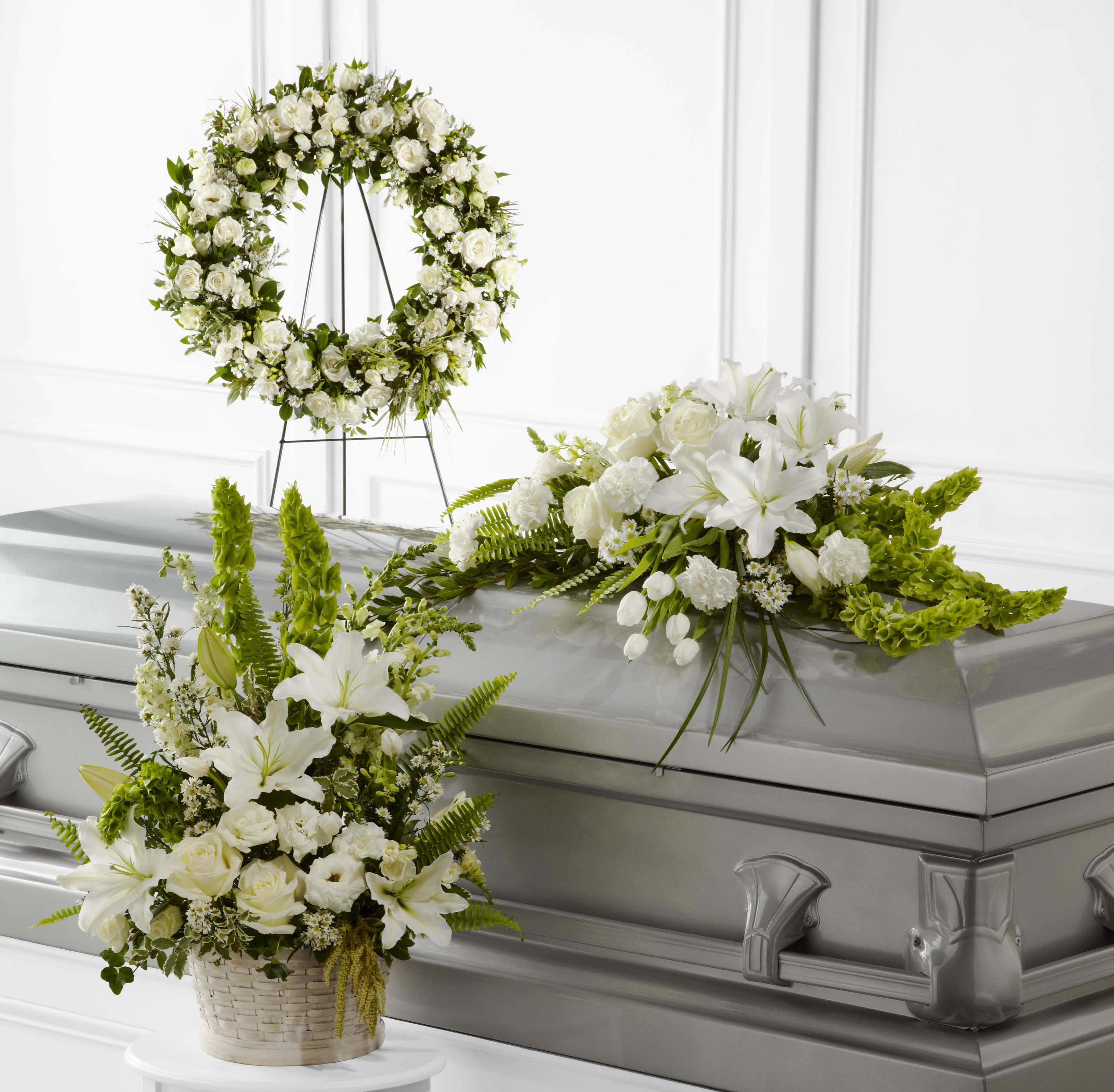White floral casket spray, wreath, and basket arrangement with lilies and roses