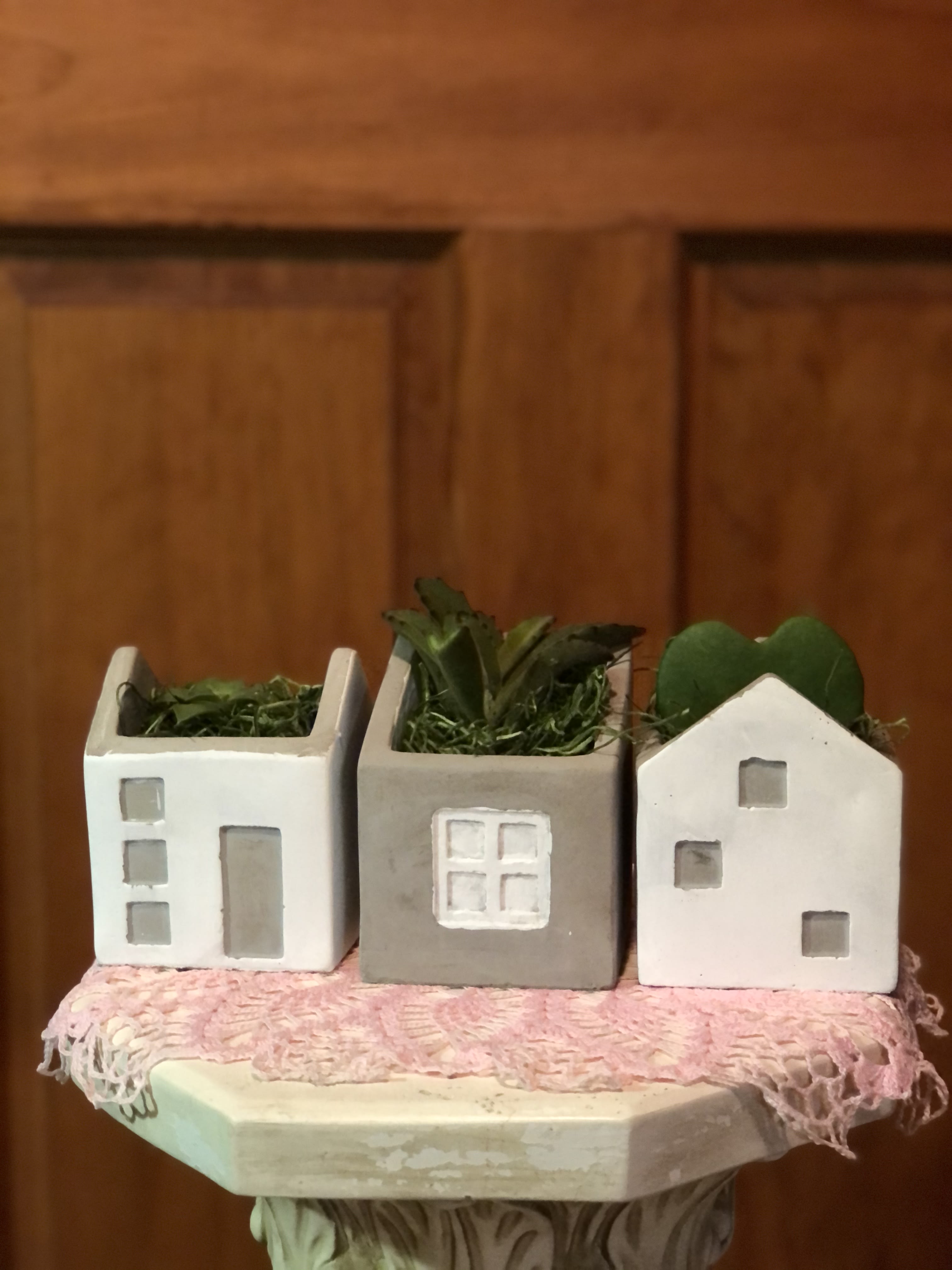 Three small house-shaped planters with succulents on a pink cloth