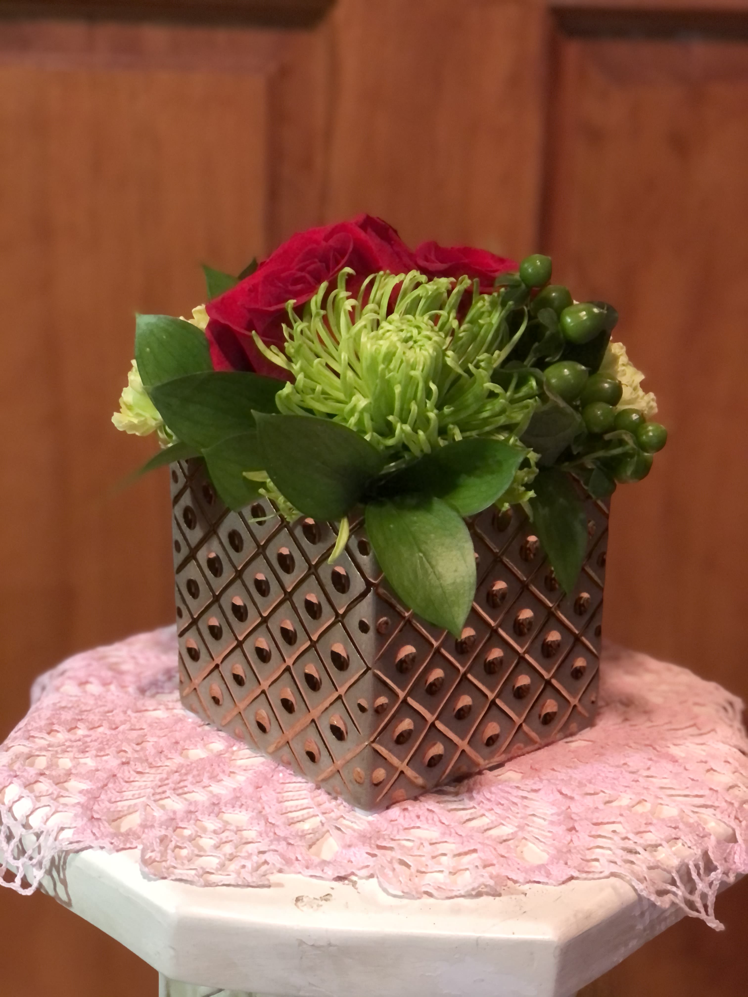 Compact floral arrangement in a patterned metal container with red and green blooms