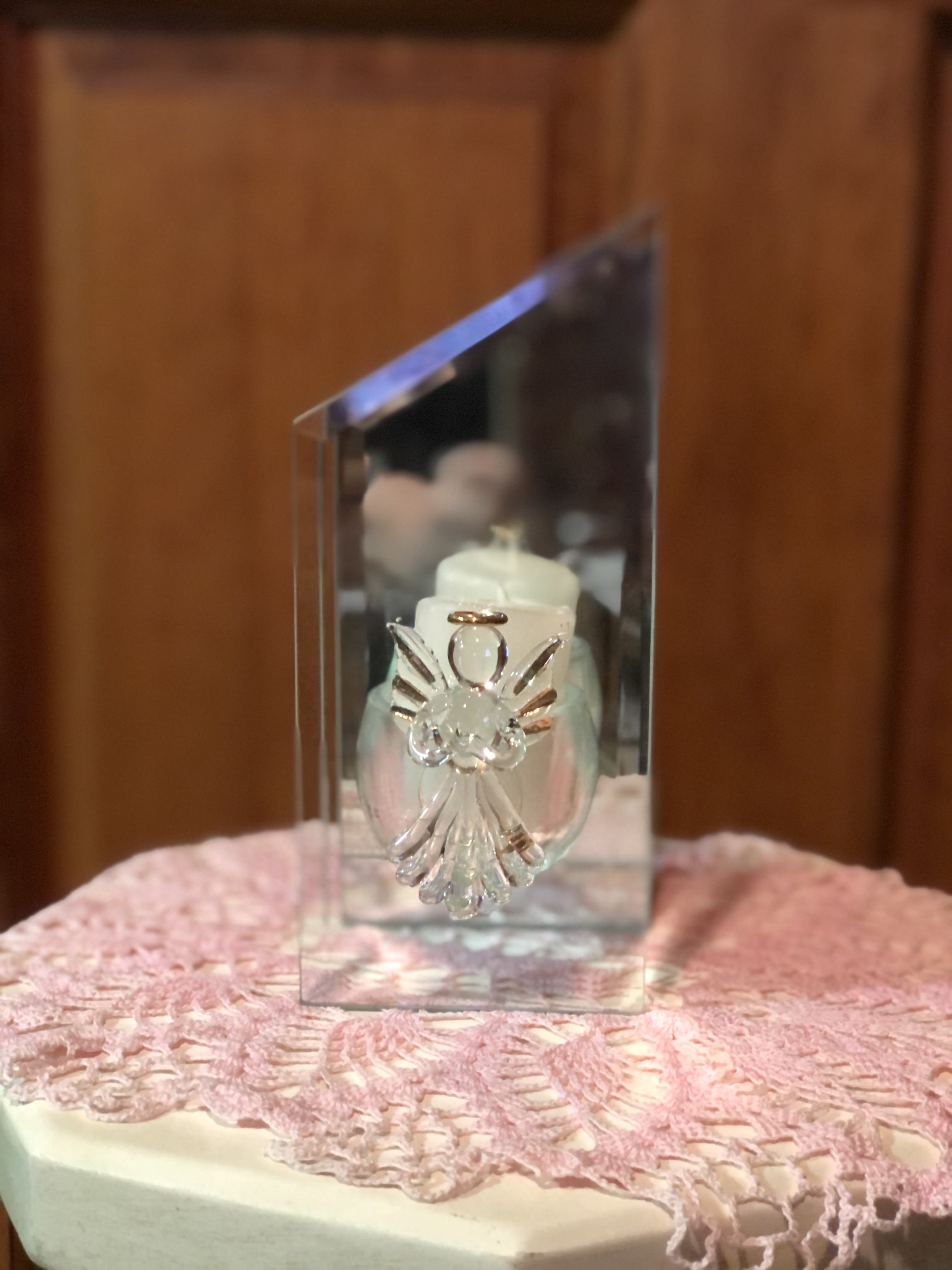 Clear glass candle holder with an angel decoration on a pink lace cloth