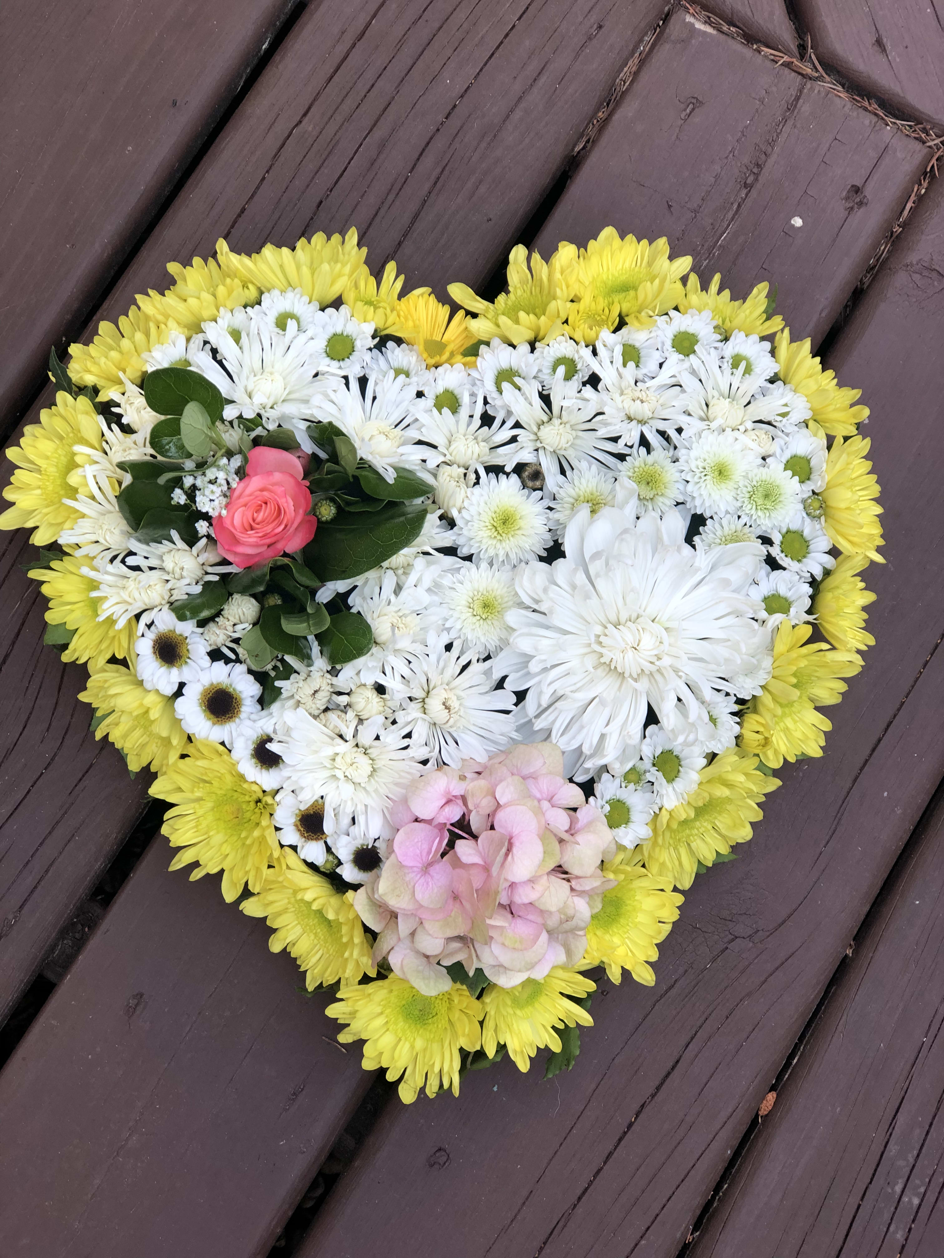 Heart-shaped floral arrangement with yellow, white, pink, and green blooms