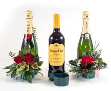 Two champagne bottles with red rose arrangements and greenery