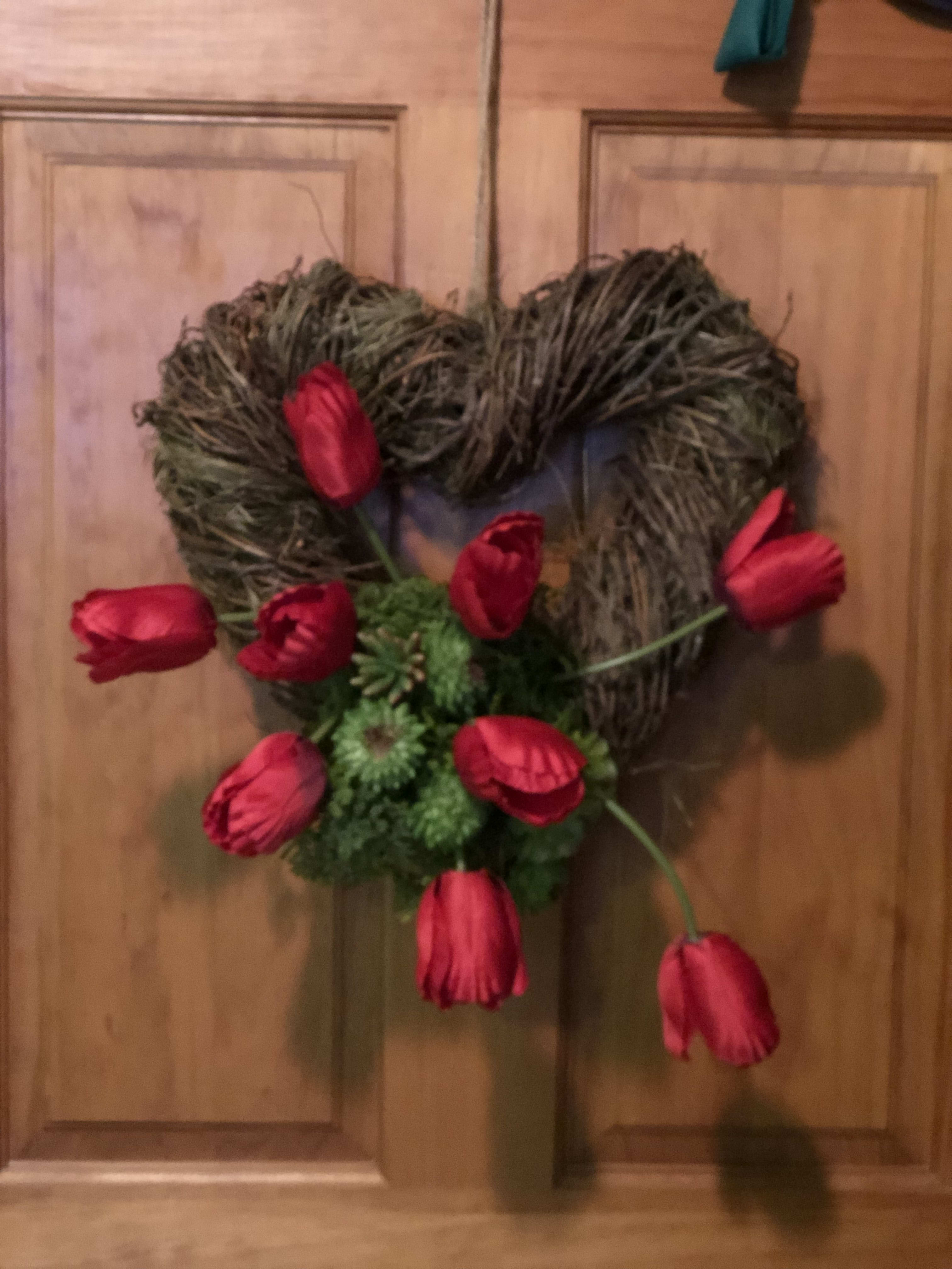 Heart-shaped twig wreath with red tulips on a wooden door