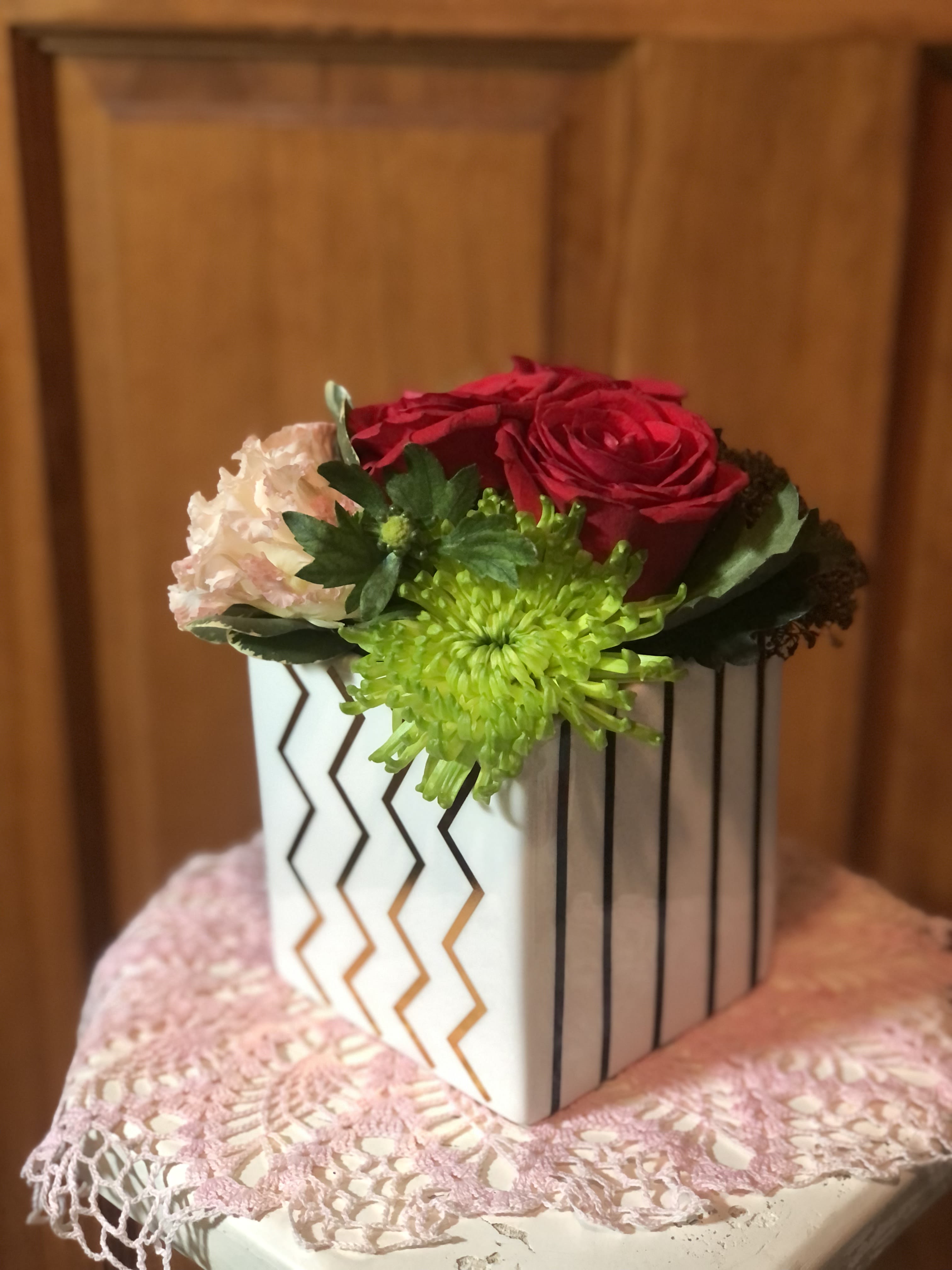 Small floral arrangement in a white geometric box with red, pink, and green blooms