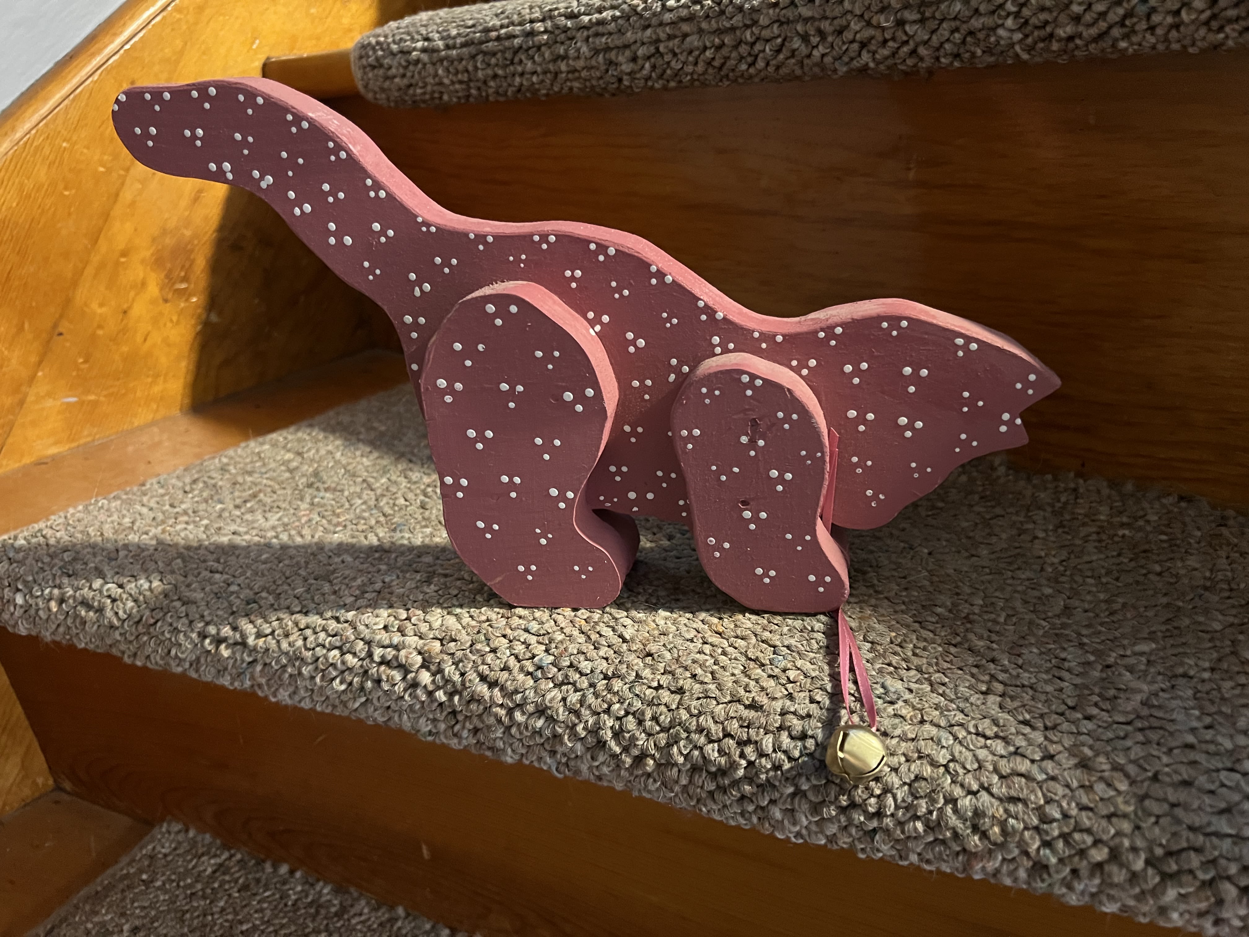 Pink wooden dinosaur decoration with white dots and a small bell