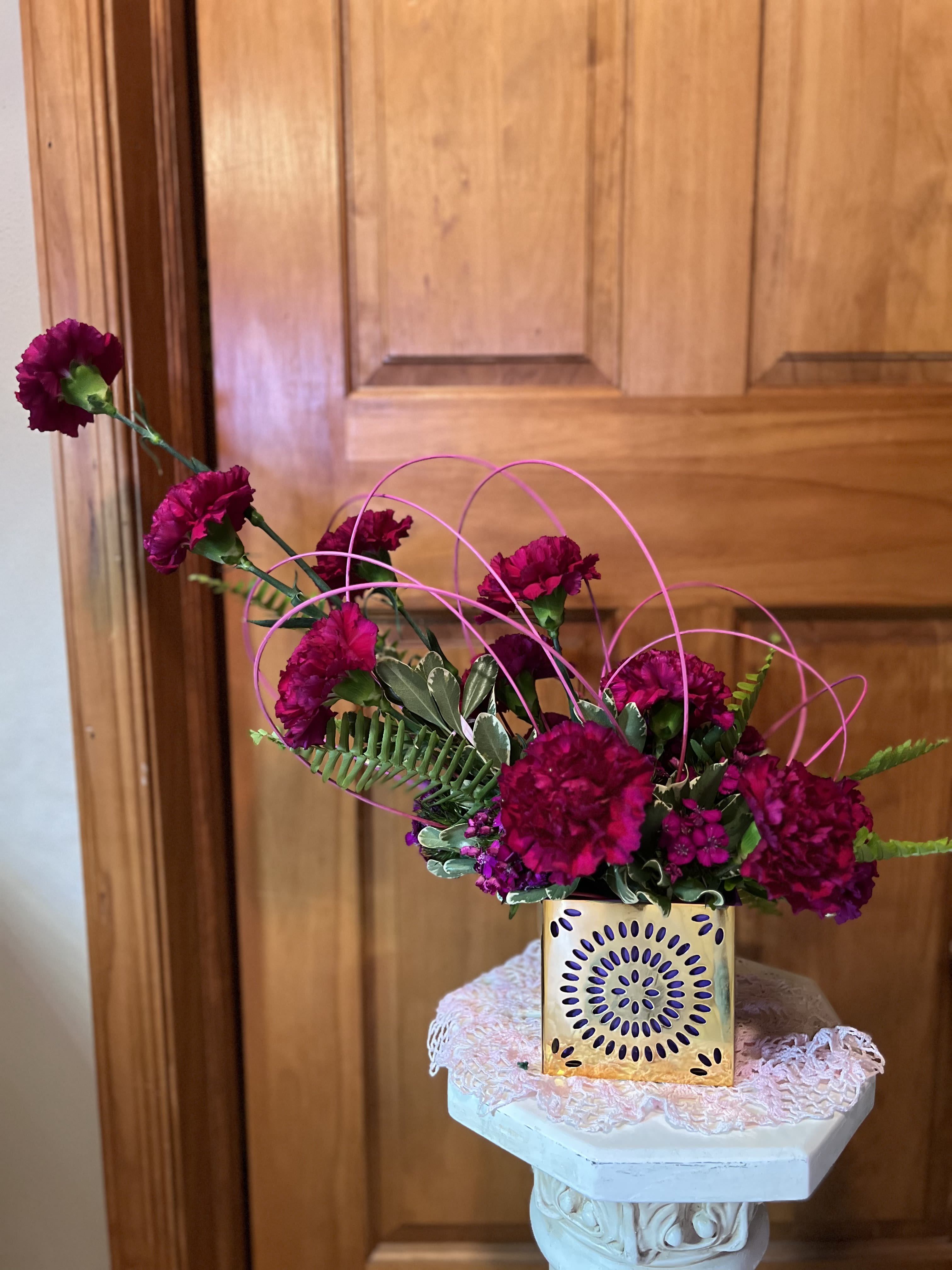 Magenta carnations in a gold square vase with pink wire loops