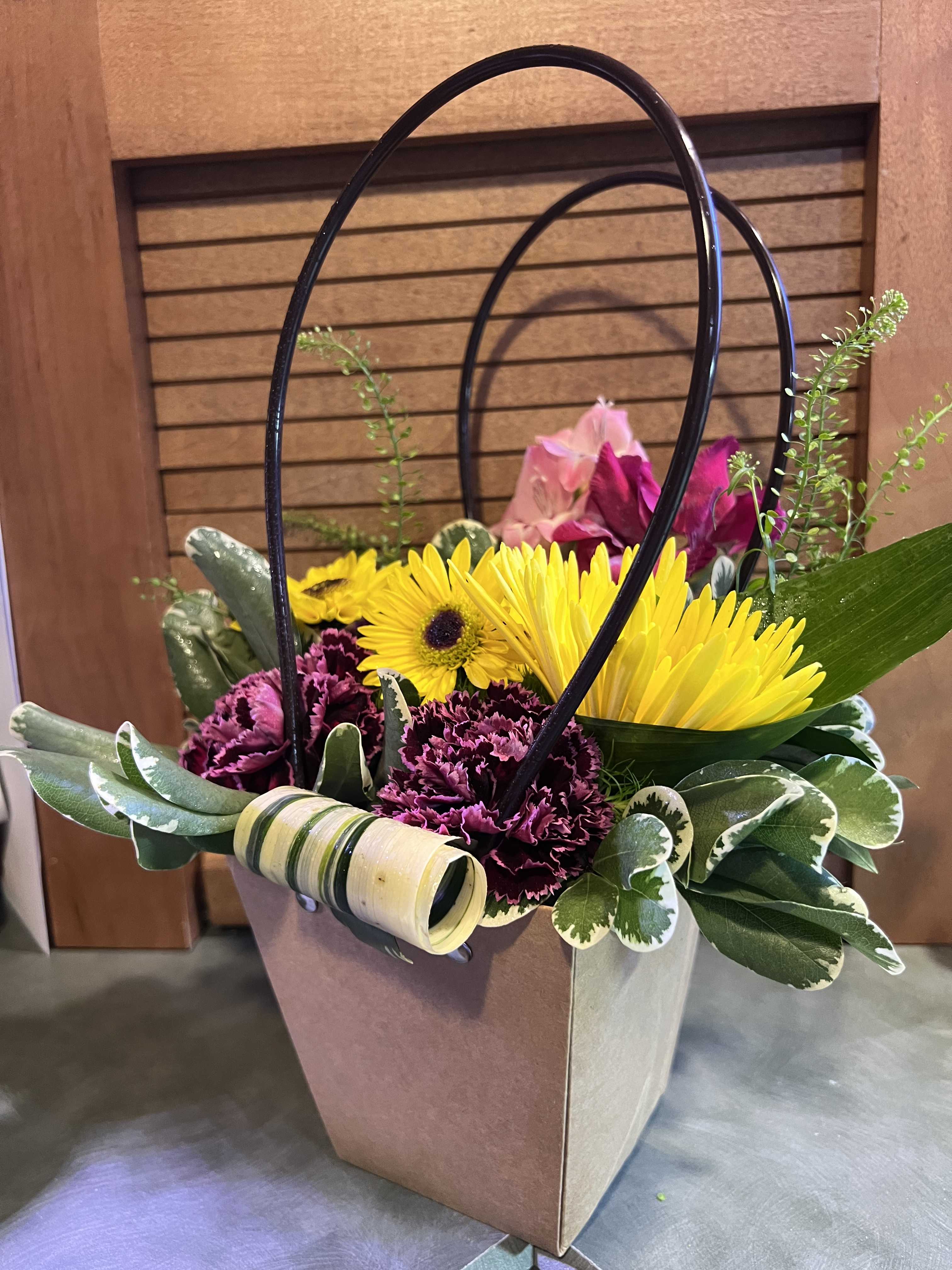 Basket arrangement with yellow gerbera daisies and purple carnations
