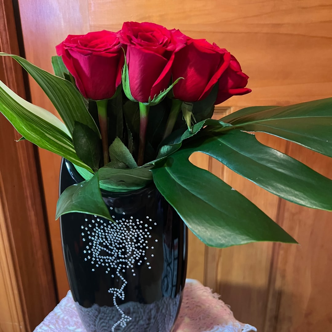 Red roses arranged in a black vase with broad green leaves.
