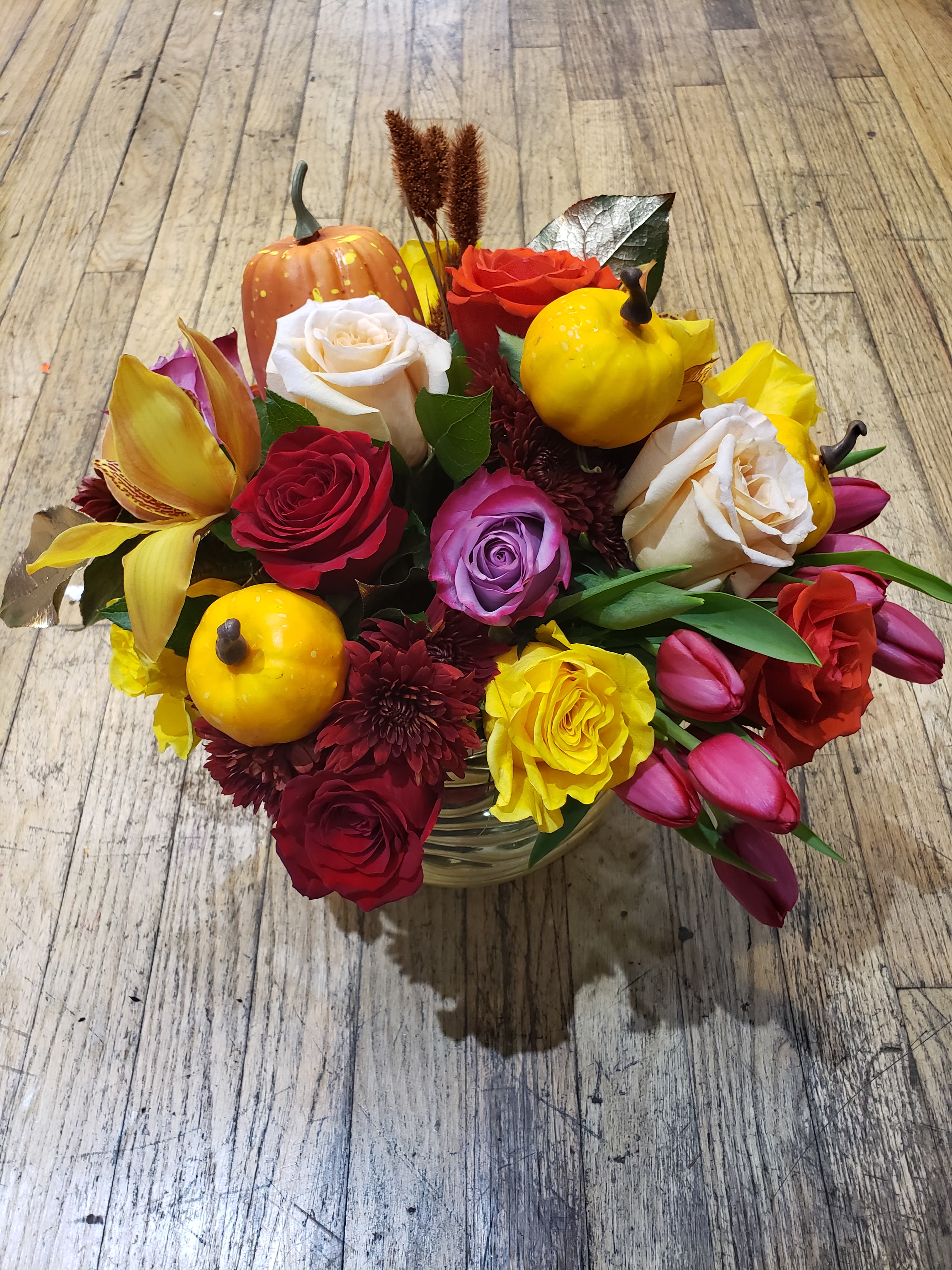 Mixed bouquet with roses, tulips, and small pumpkins in a glass vase