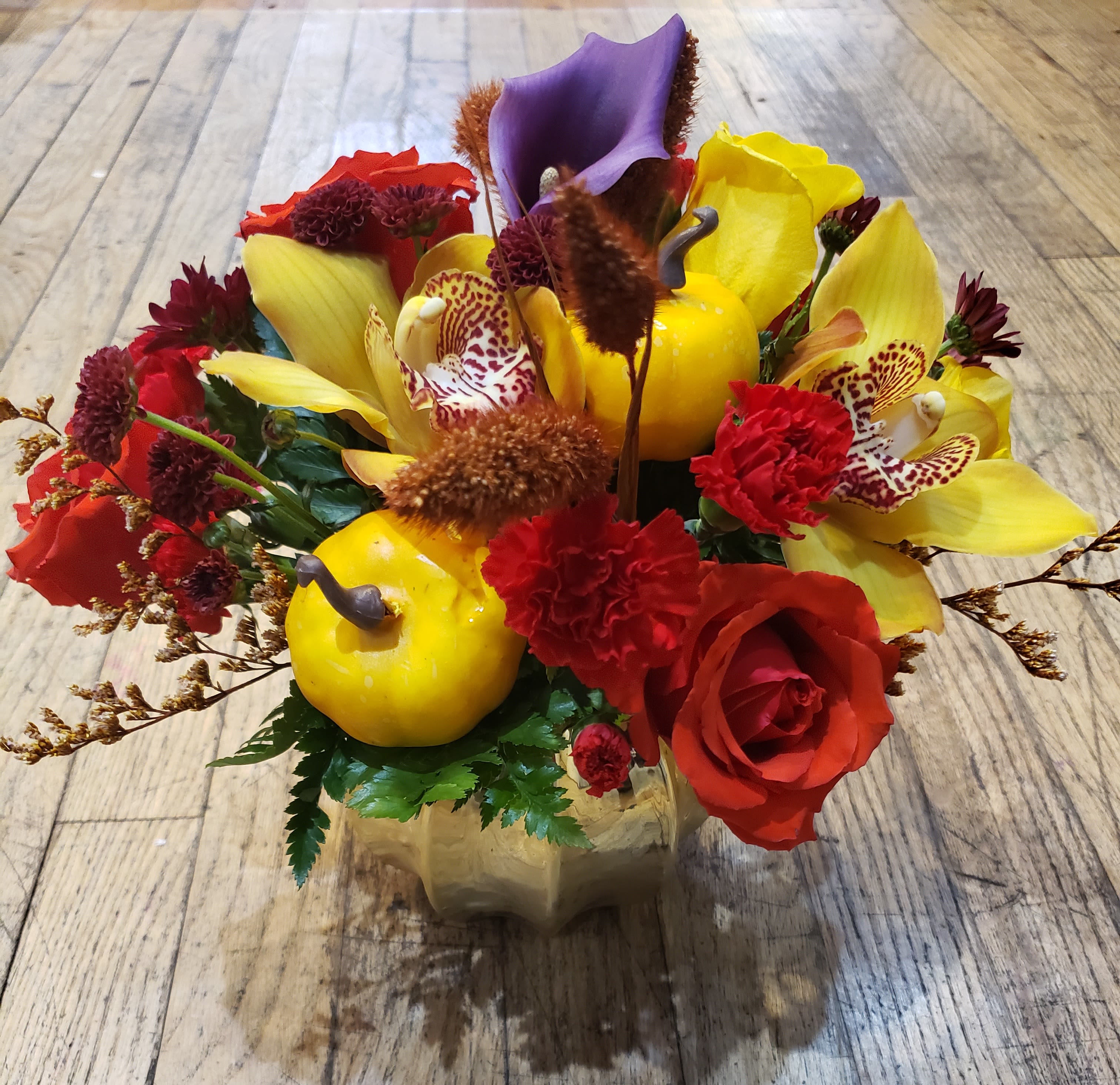 Colorful floral arrangement with roses, calla lilies, and orchids in a gold vase