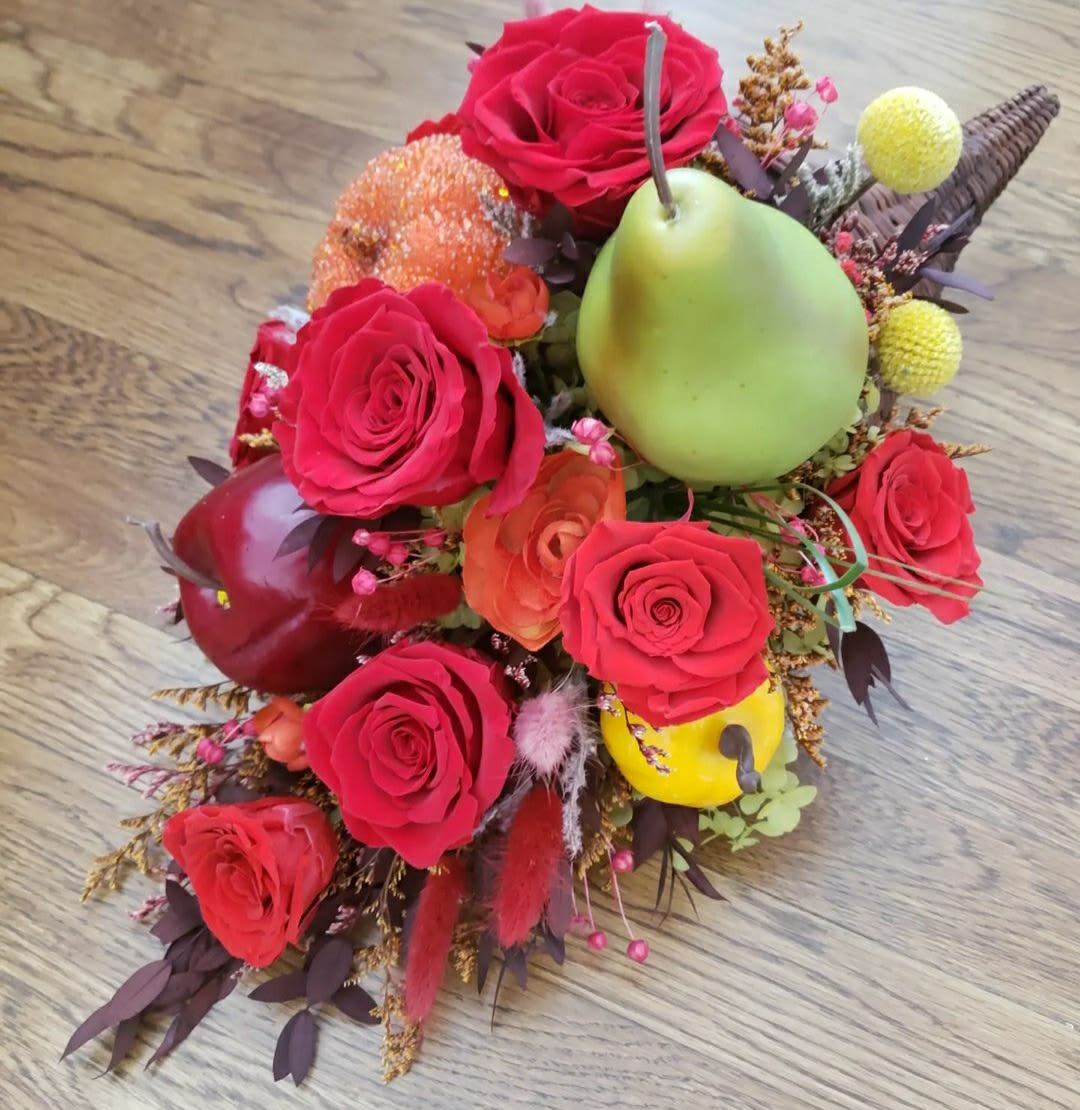 Red roses arranged with decorative fruit accents on a wooden surface