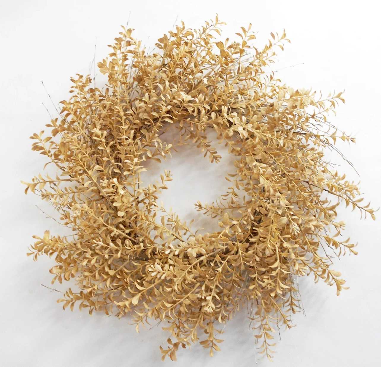 Dried golden wreath with small clustered leaves on a white background