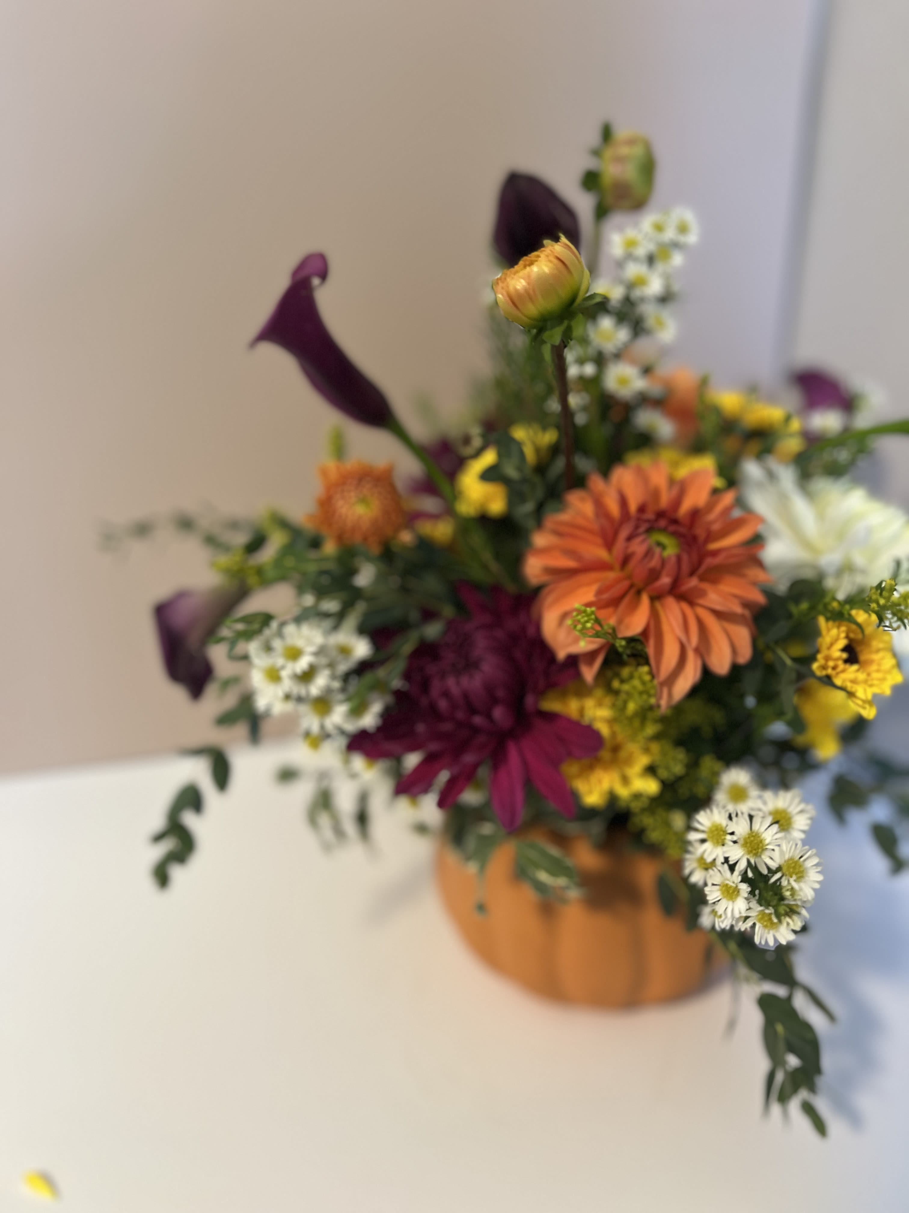 Mixed bouquet with orange, purple, white, and yellow flowers in a pumpkin-shaped container