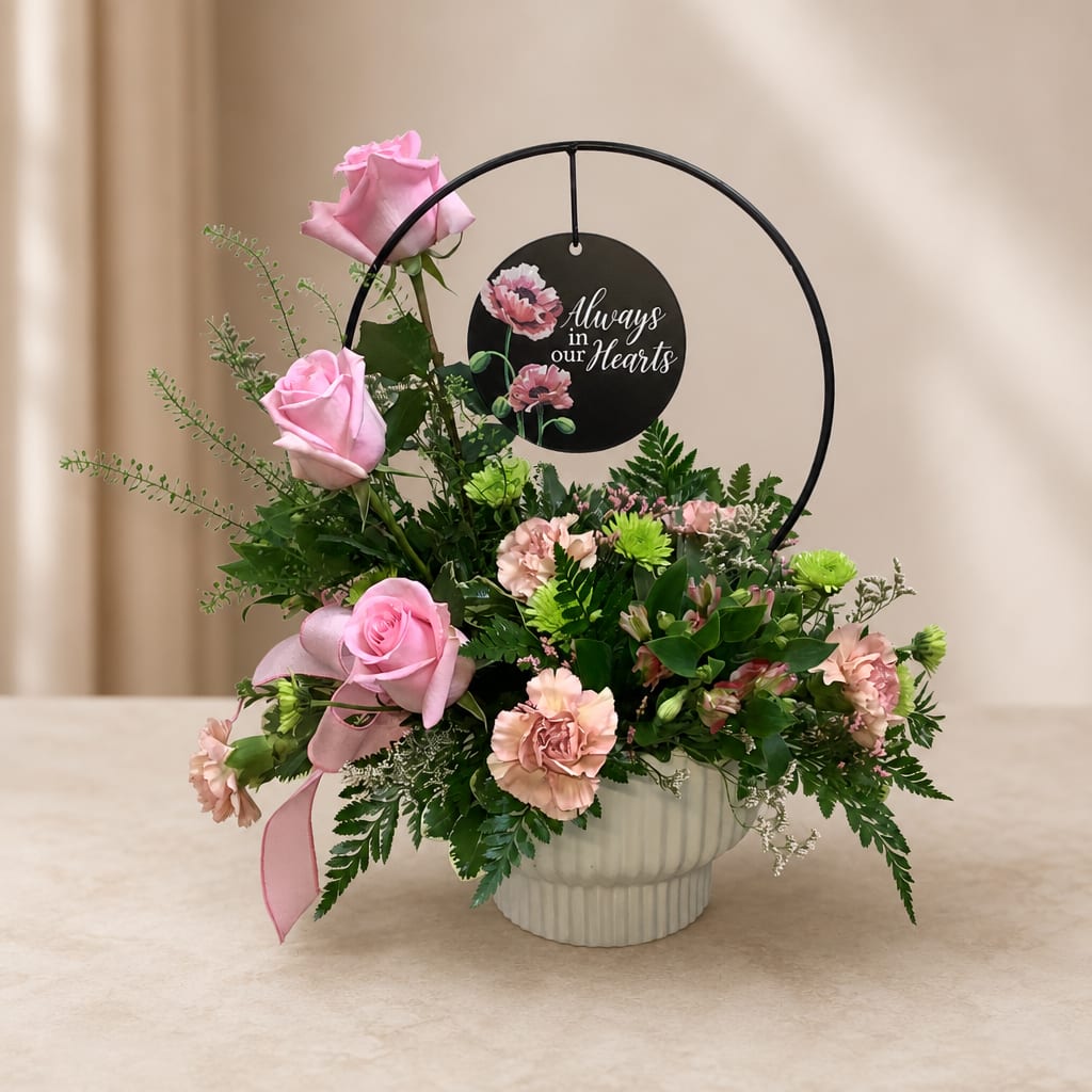 Pink roses and carnations in a white vase with a memorial sign