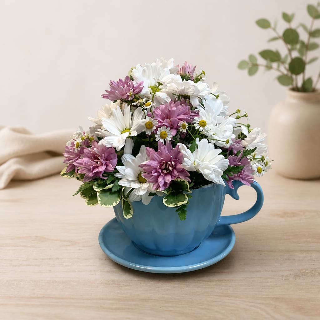 White and lavender daisies arranged in a blue teacup with saucer