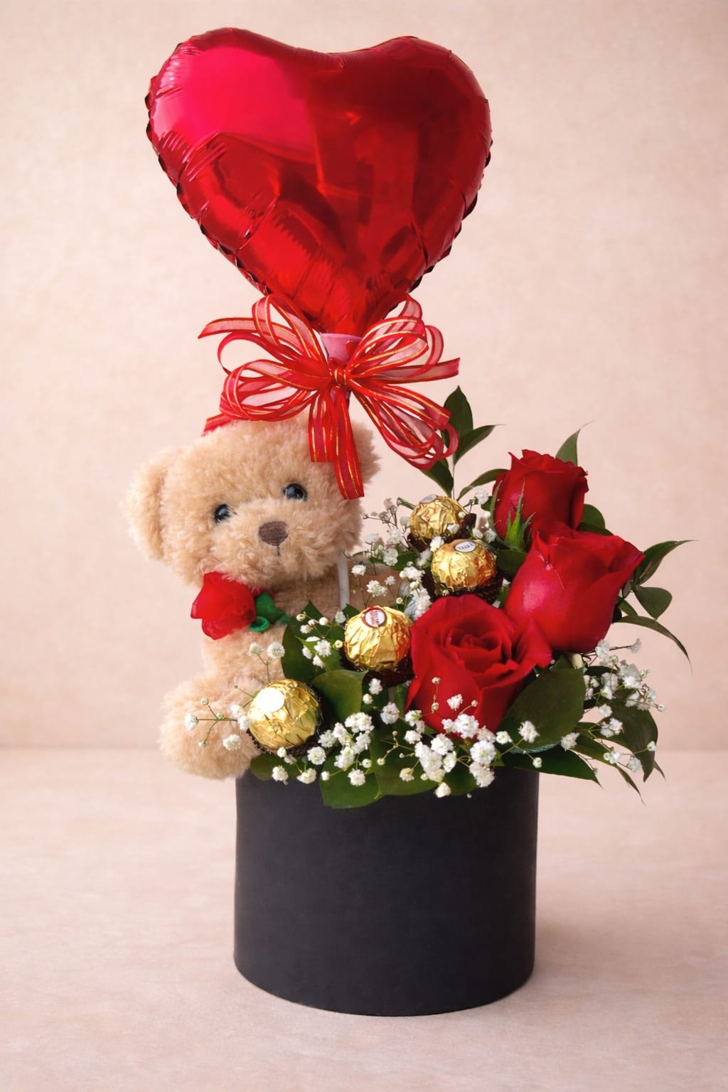 Teddy bear gift arrangement with red roses, chocolates, and a heart balloon