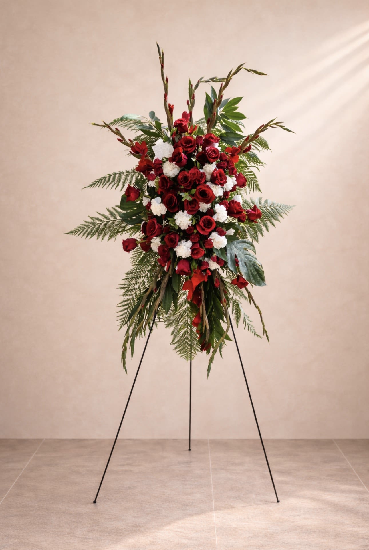 Eternal Red Tribute - A graceful standing floral tribute designed with premium red roses, white carnations, tropical foliage, and elegant greenery to honor and celebrate a beautiful life with love and respect.