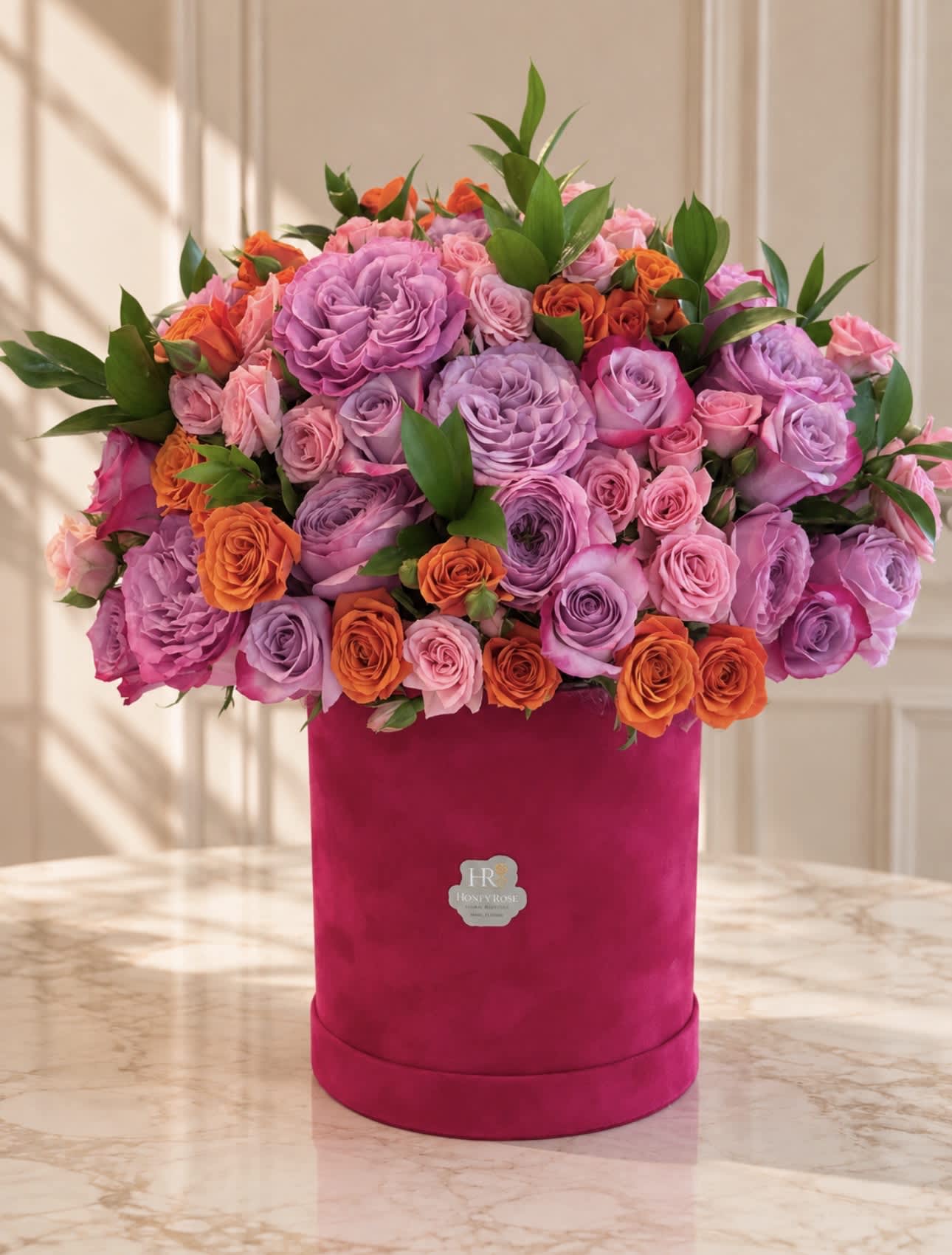 Pink and lavender roses arranged in a magenta hat box