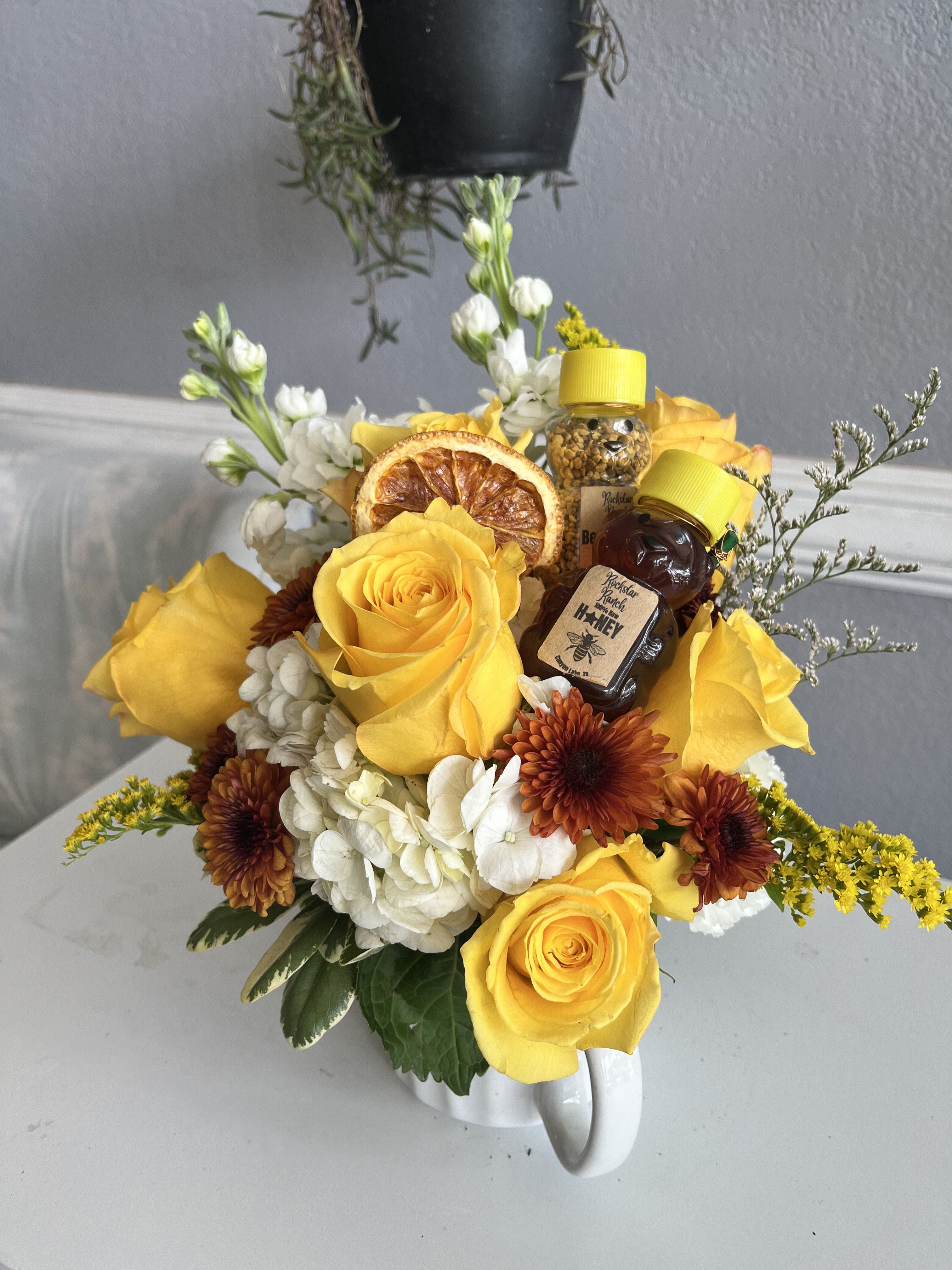 Yellow roses and white flowers arranged in a white mug with honey jars