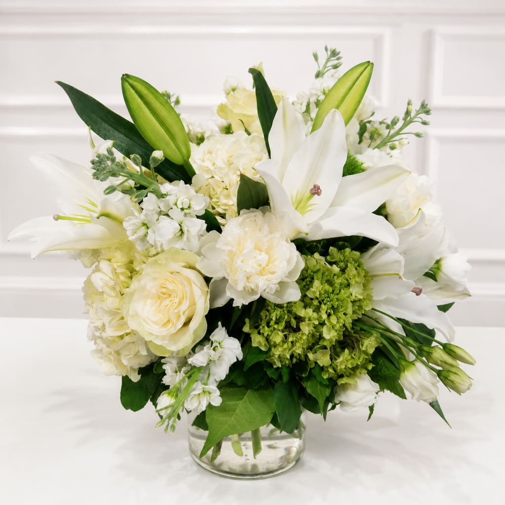 White lilies and cream roses arranged in a clear glass vase