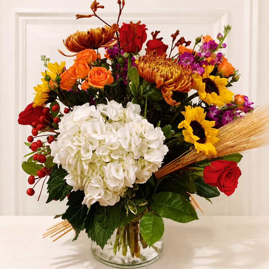 Mixed bouquet with white hydrangea, red roses, sunflowers, and orange blooms in a glass vase