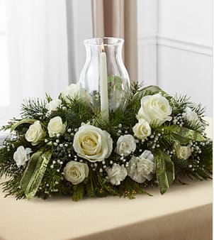 Glowing Elegance™ Centerpiece - The FTD® Glowing Elegance™ Centerpiece brings a warm sophistication to your holiday table with each snow-kissed bloom. White roses, spray roses, carnations, mini carnations and baby's breath are beautifully arranged amongst an assortment of lush holiday greens to create an incredible winter holiday display. With a glass hurricane at the center of this fresh flower arrangement holding a single white taper candle, this centerpiece is beautifully accented with a sheer green sparkle ribbon to create a stunning holiday gift for your favorite special recipient, or home accent for your own Christmas gathering. BETTER centerpiece is approximately 7"H x 20"W x 13"D. Your purchase includes a complimentary personalized gift message.