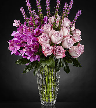 Pink roses and purple orchids in a clear glass vase