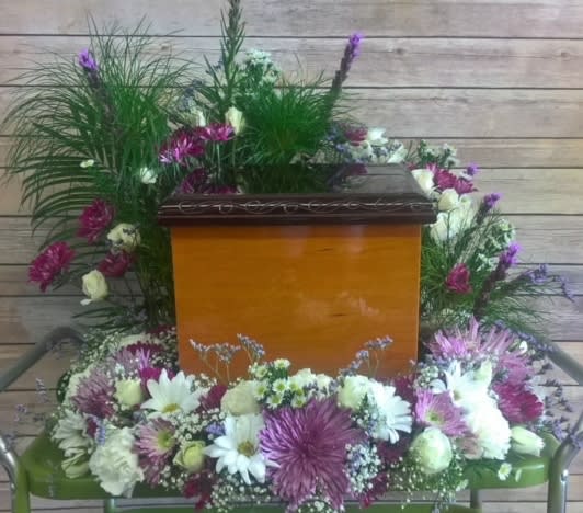 Casket surrounded by white and purple floral sprays