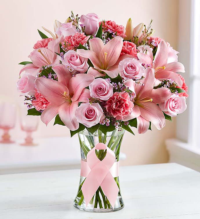 Pink lilies and roses arranged in a clear glass vase with a pink ribbon