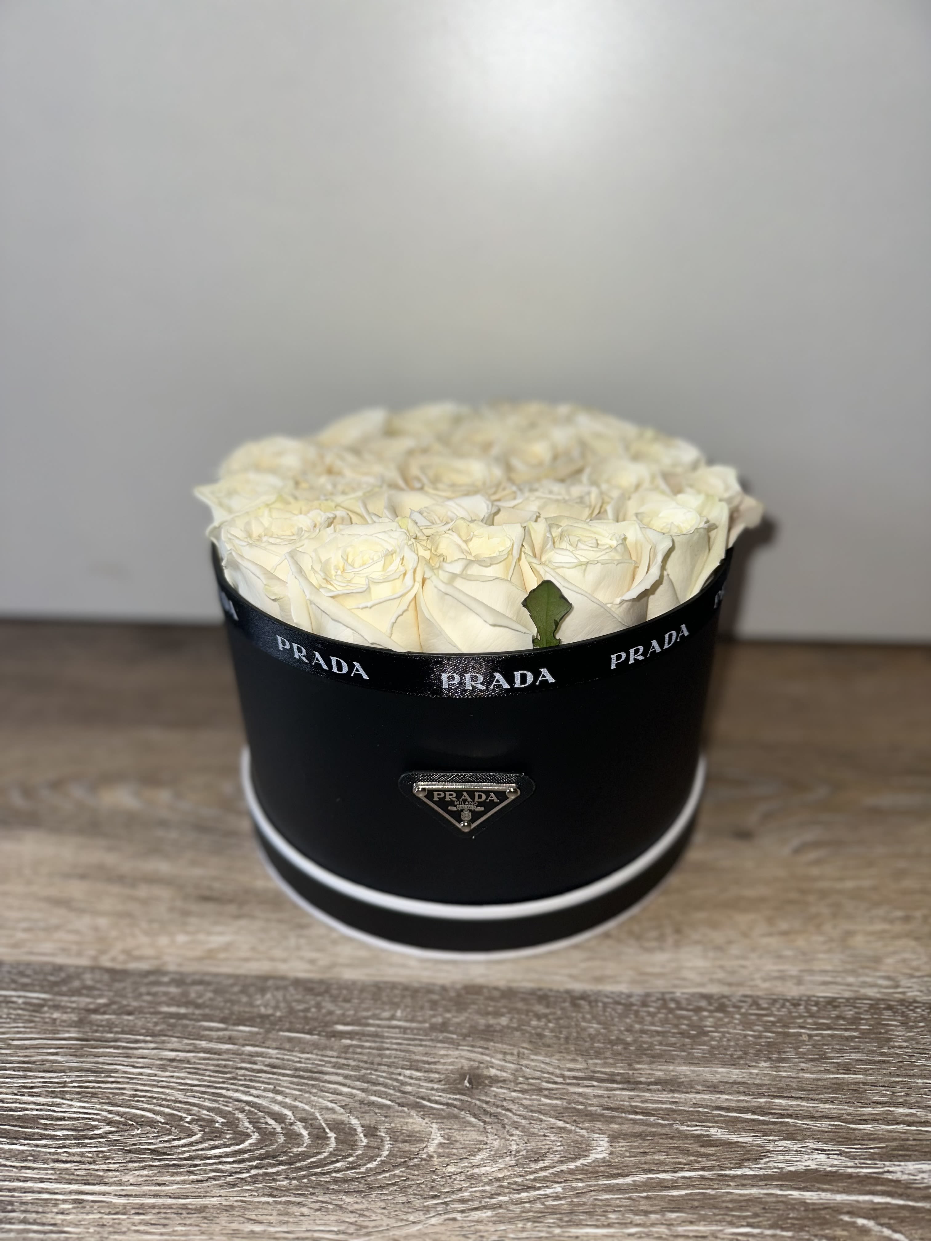 Cream roses arranged in a black round box with Prada branding