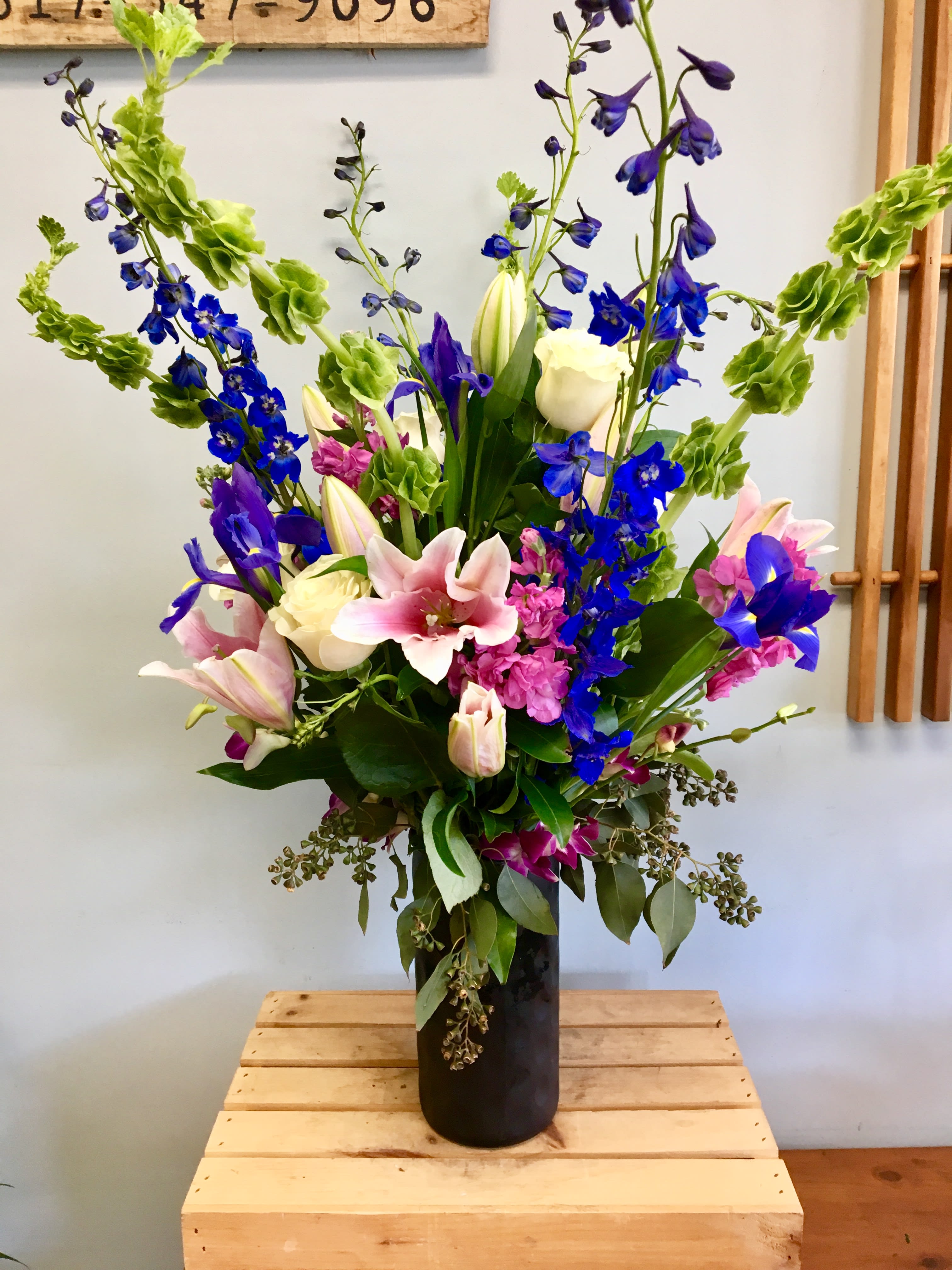 Tall mixed bouquet with pink lilies, blue delphinium, and white roses in a black vase