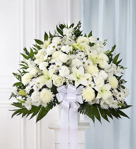 Large white floral arrangement with lilies, roses, and a white bow in a vase.