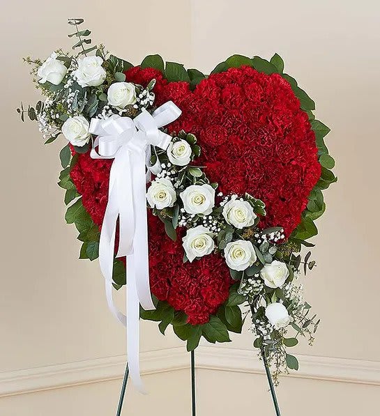Standing heart-shaped spray of red carnations with white roses and bow on an easel